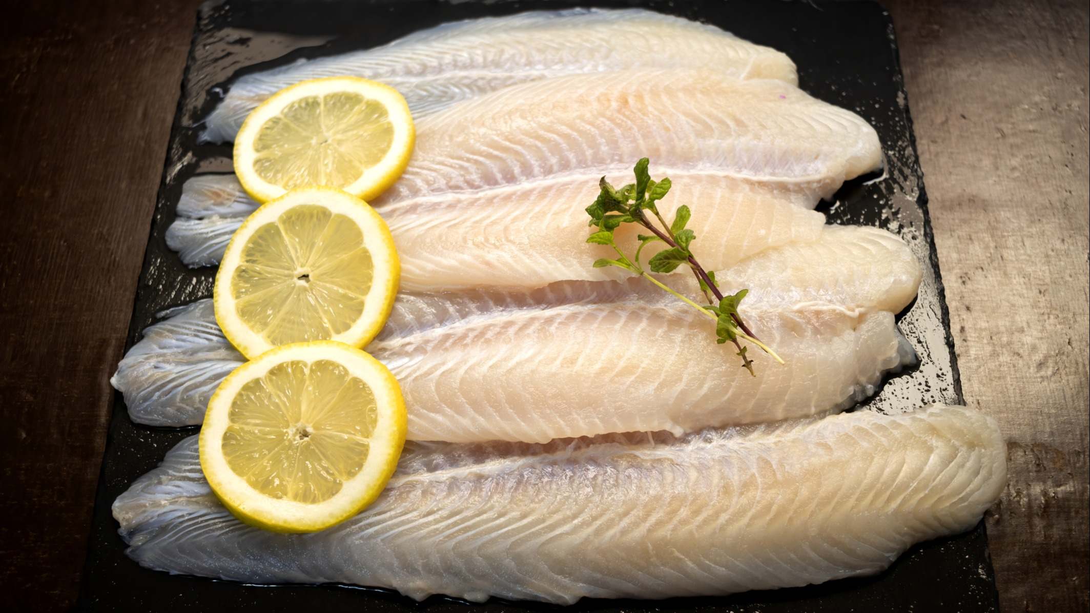 Filetes de panga, pescado blanco de Asia, con rodajas de limón y fondo oscuro