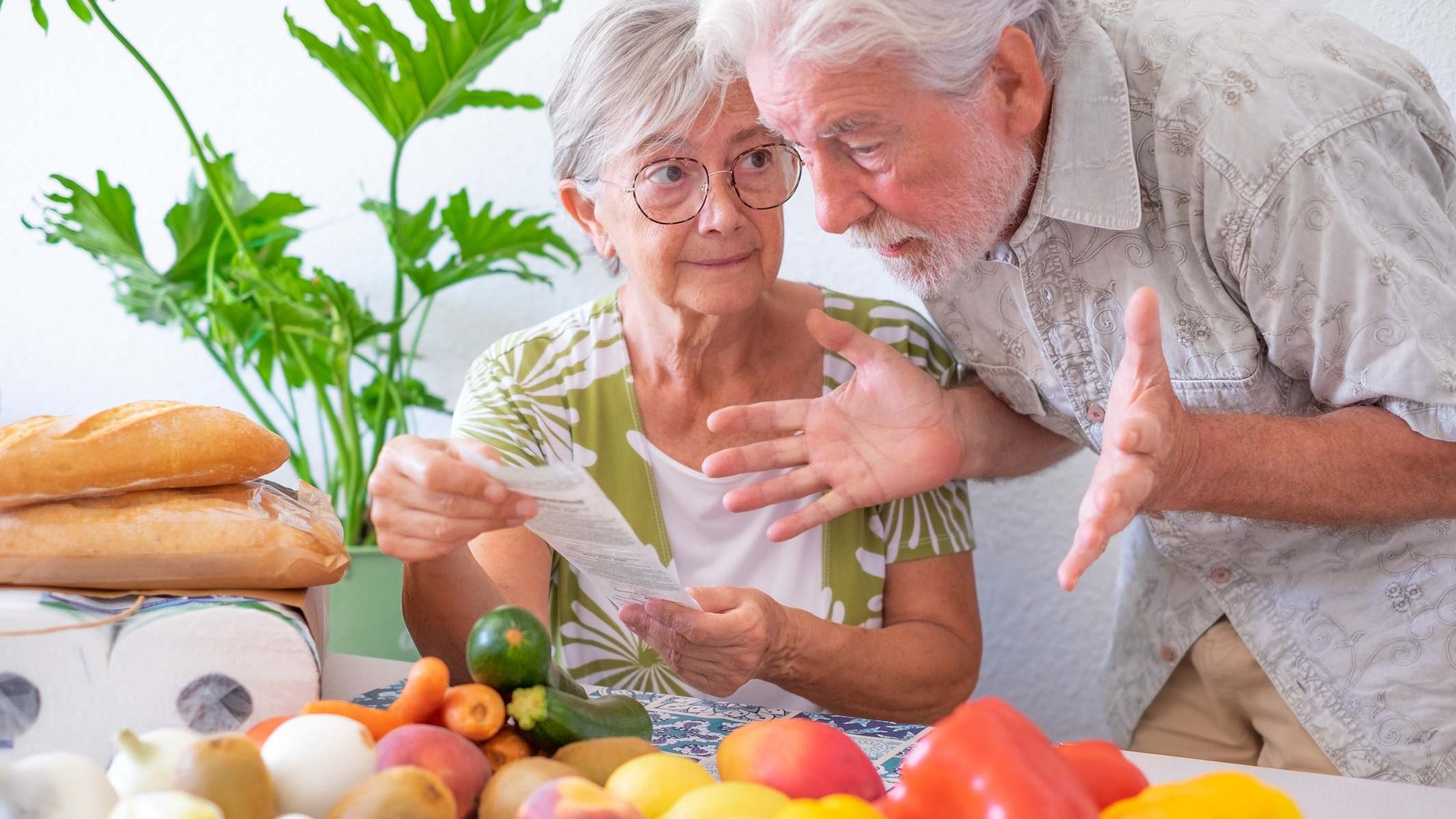 Pareja de ancianos preocupados con un ticket de compra y varios alimentos en la mesa