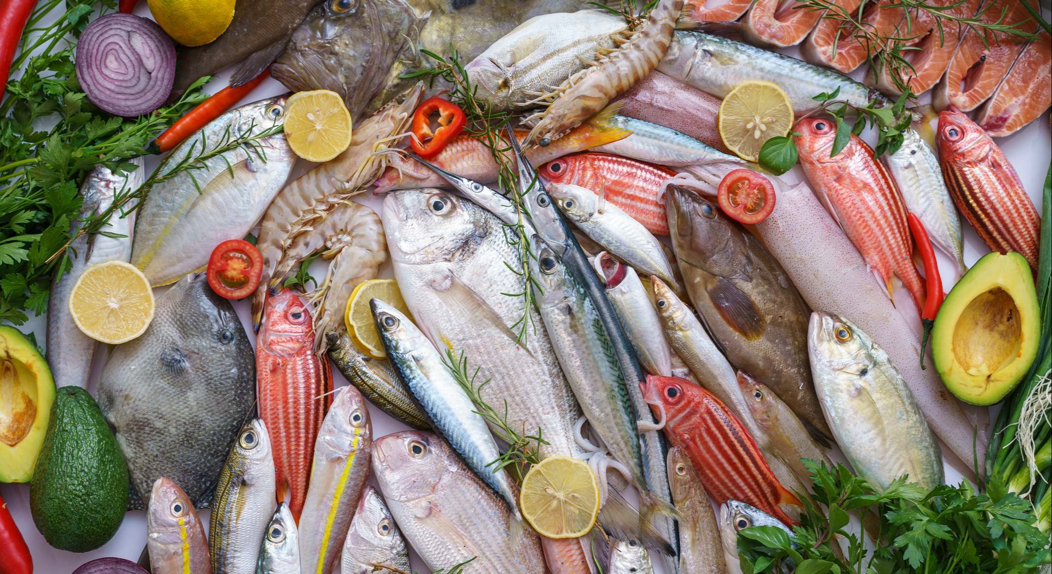 Varios pescados y mariscos frescos decorados con cubitos de hielo, rodajas de limón, hierbas y verduras