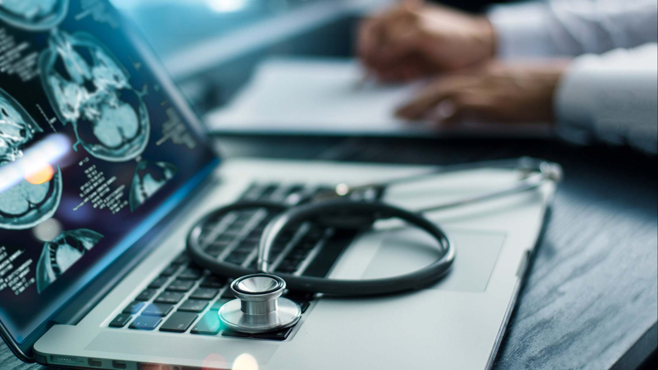 Ordenador con un estetoscopio sobre el teclado con las manos de un médico de fondo