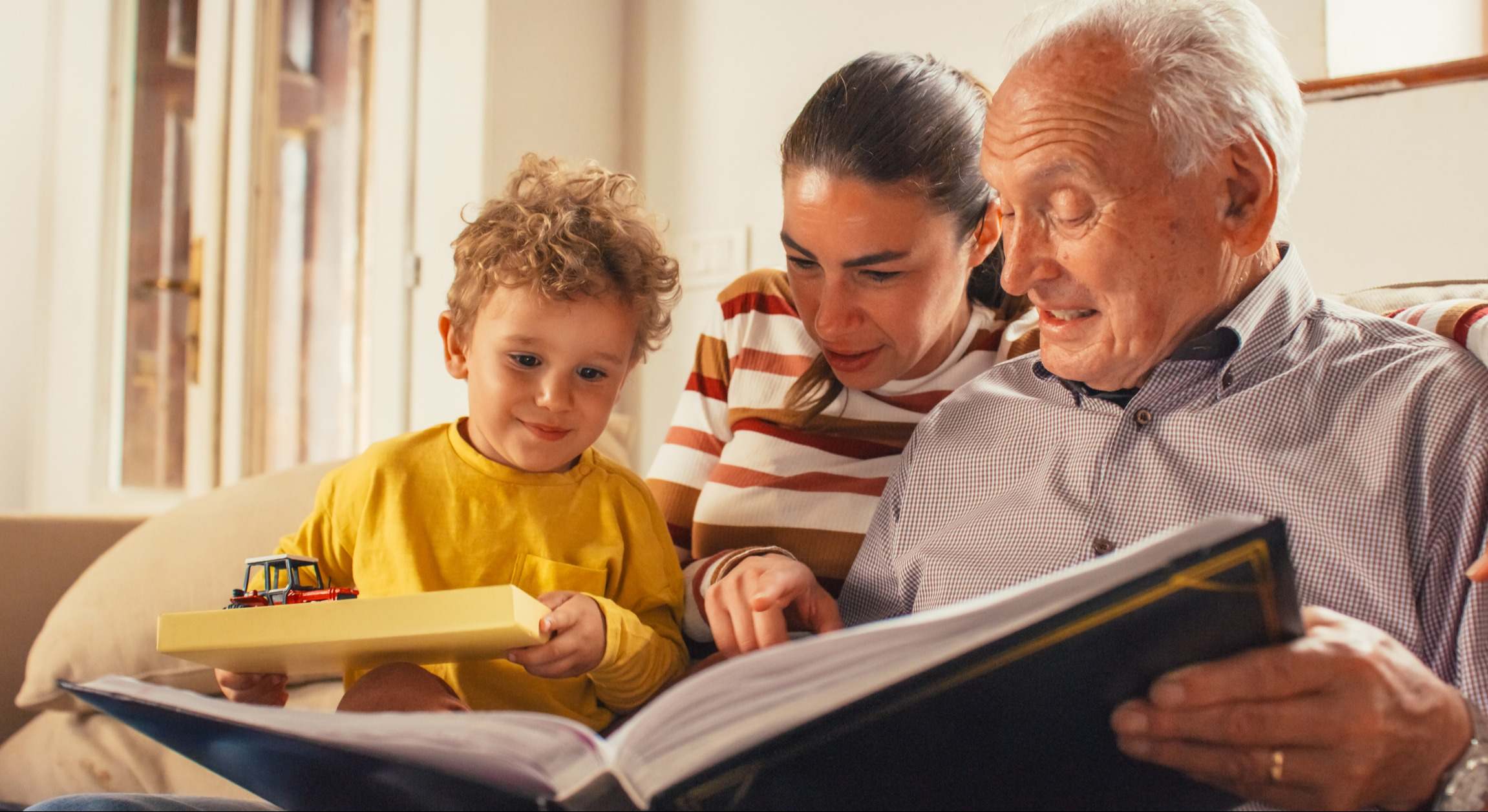 Familia formada por un abuelo, una mujer joven y un niño viendo un álbum de fotos