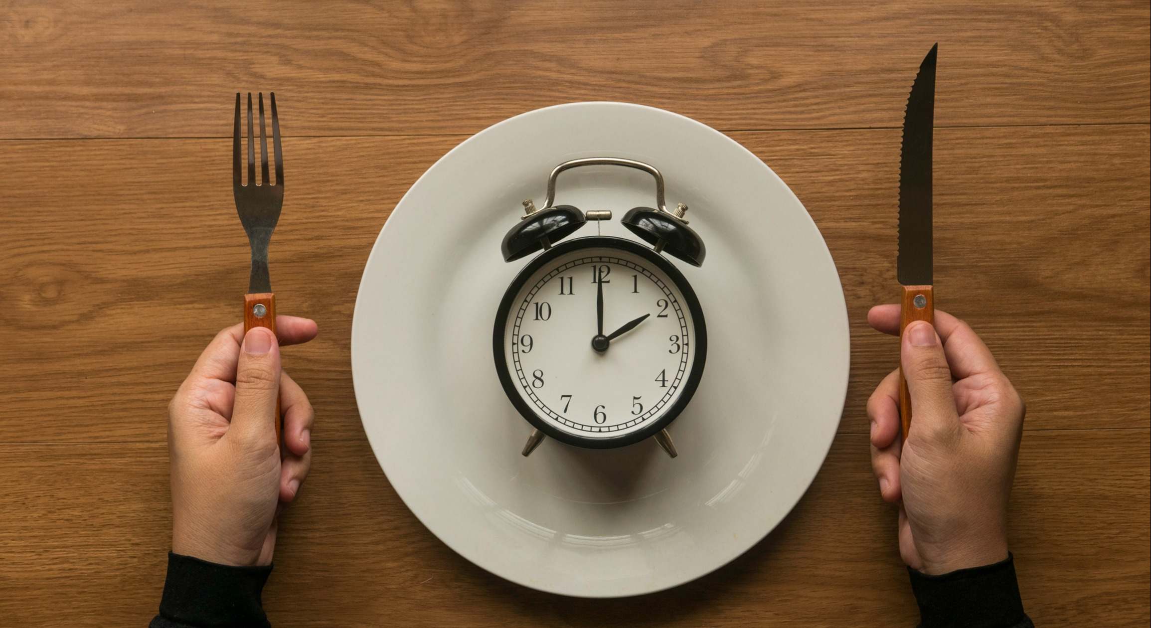 Manos sosteniendo tenedor y cuchillo y un despertador vintage en un plato blanco
