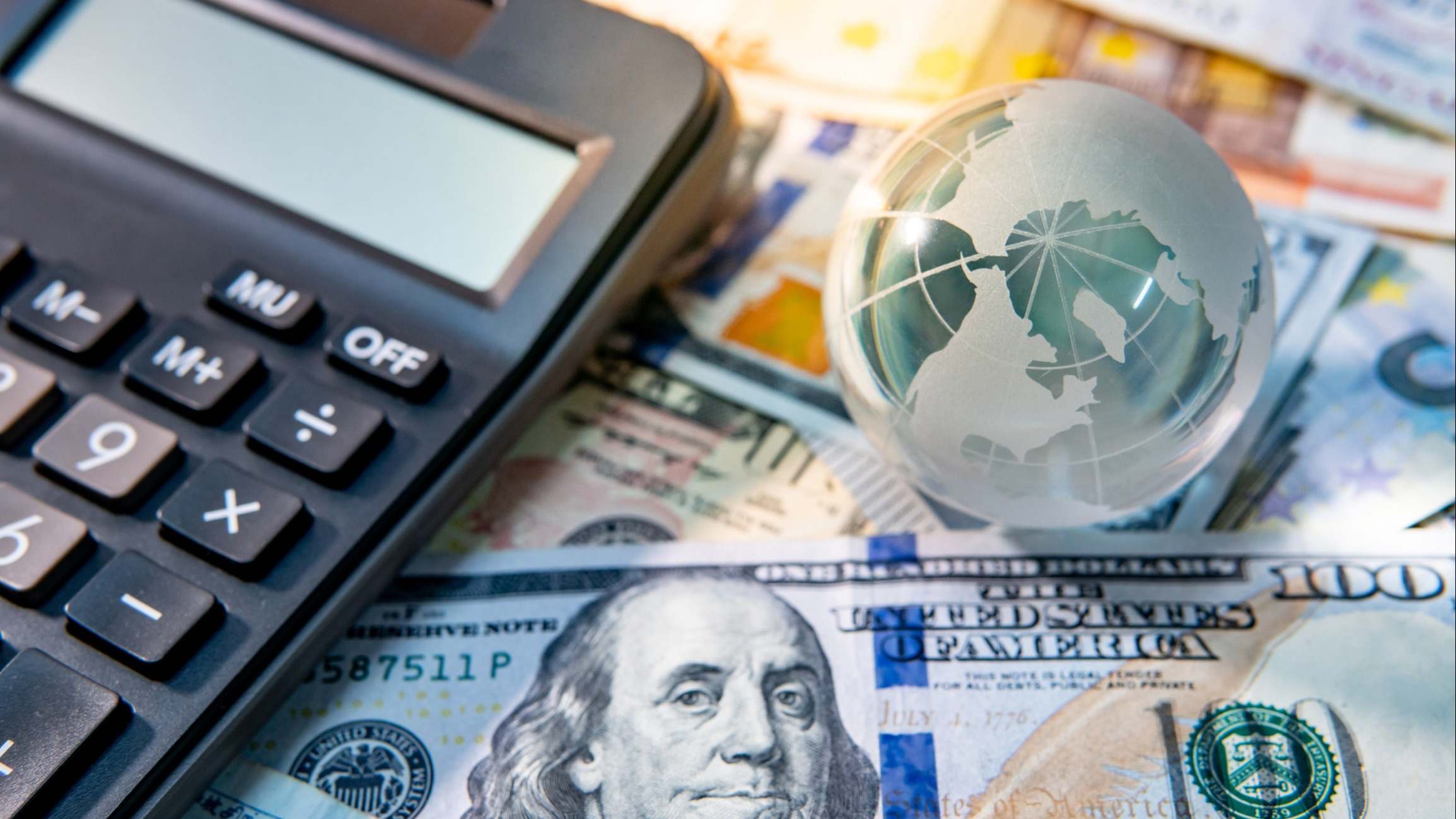 Vista de una calculadora sobre billetes y junto a una bola del mundo