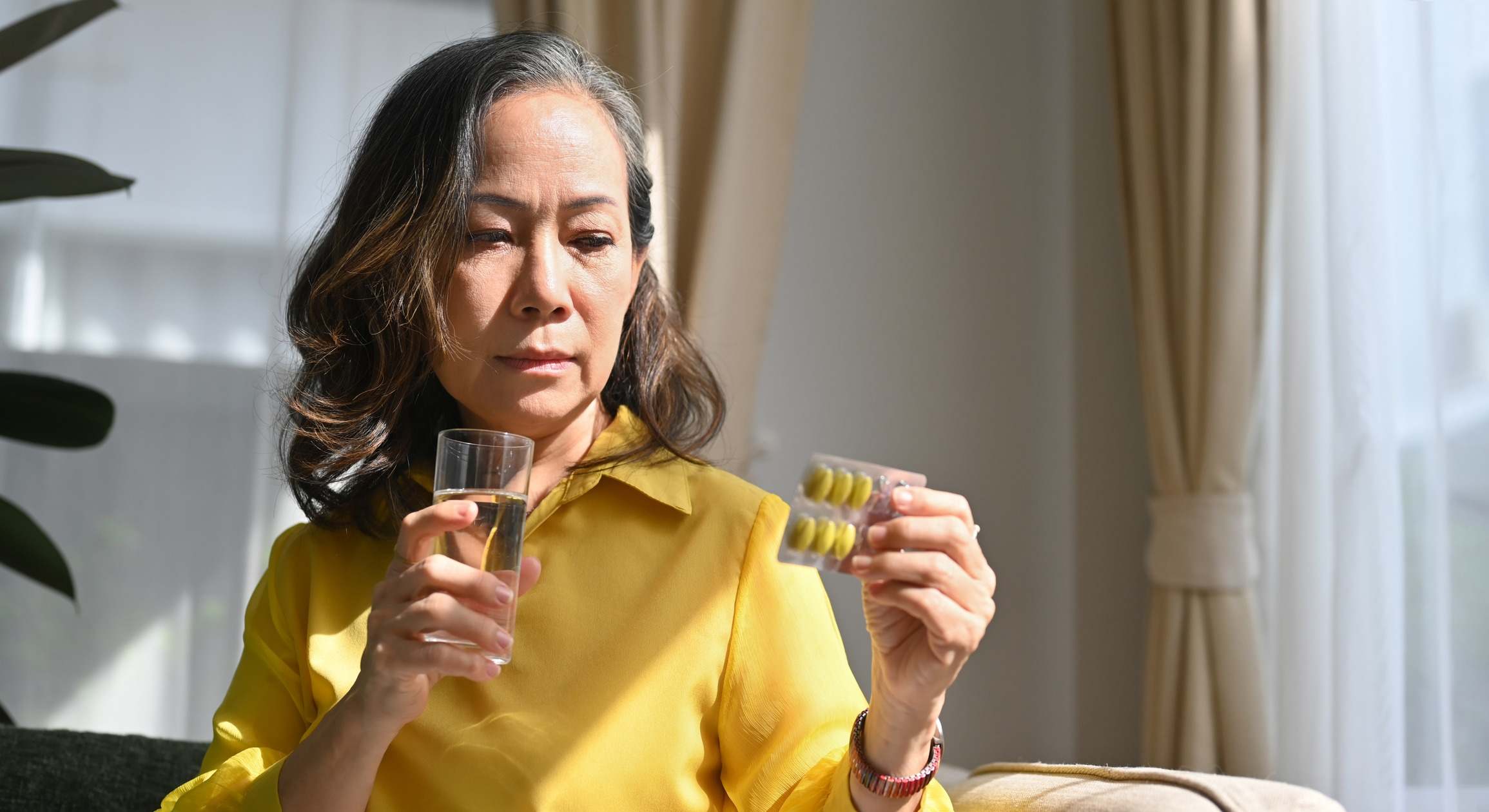Mujer sujetando una tira de pastillas en una mano y un vaso de agua en la otra