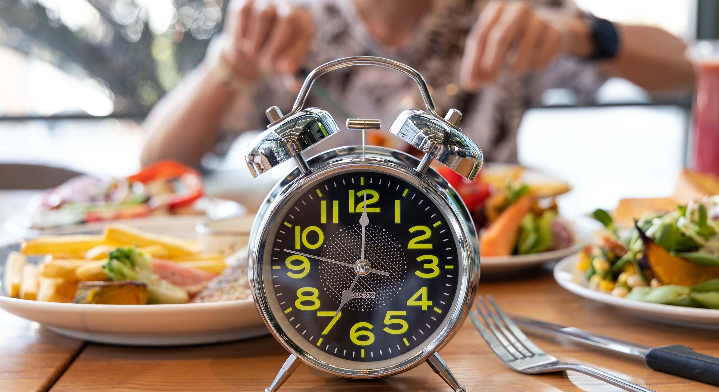 Persona comiendo en una mesa llena de platos con un reloj en primer plano