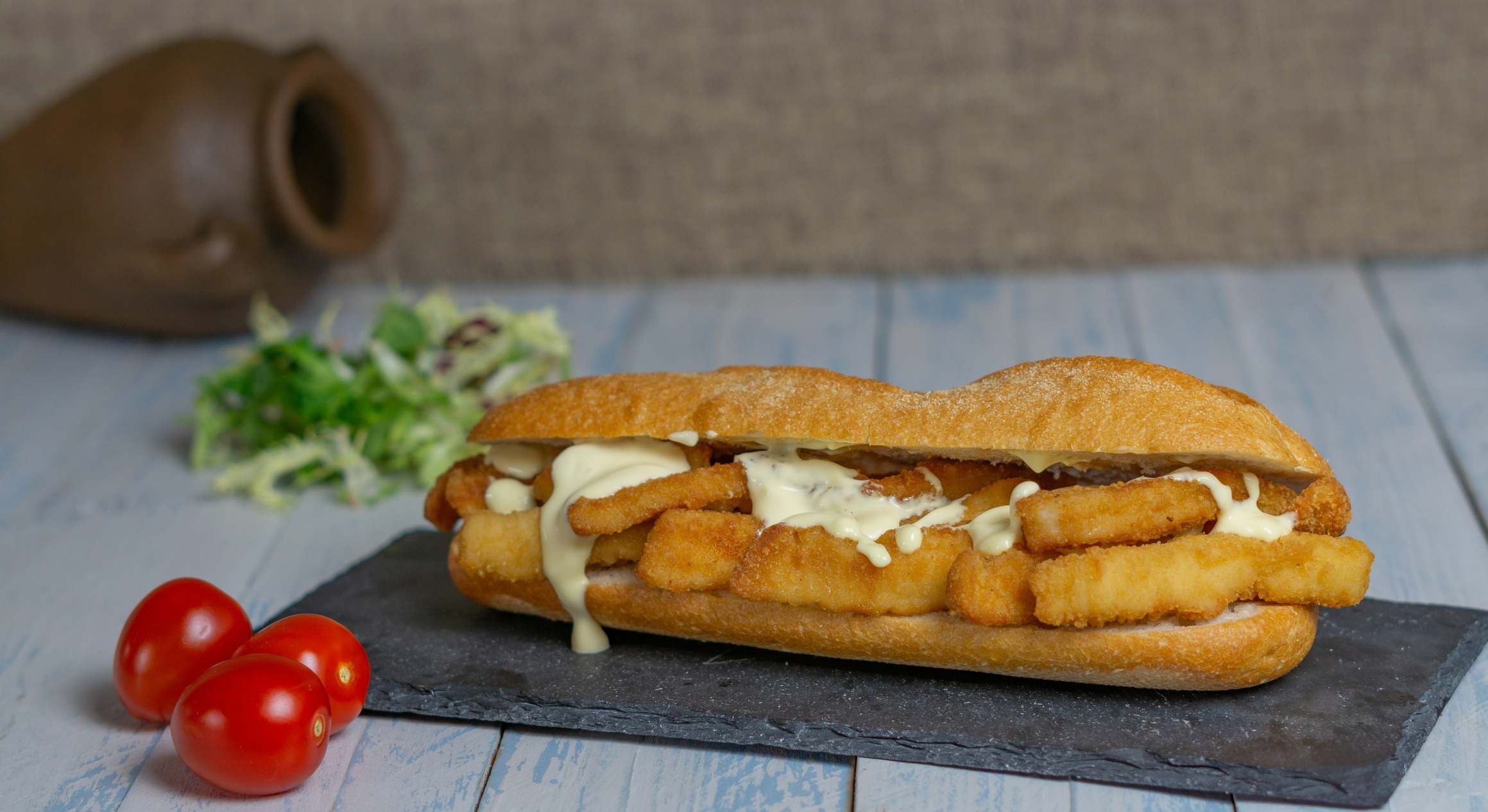 Un bocata de calamares sobre un plato de pizarra y unos tomatitos cherries al lado