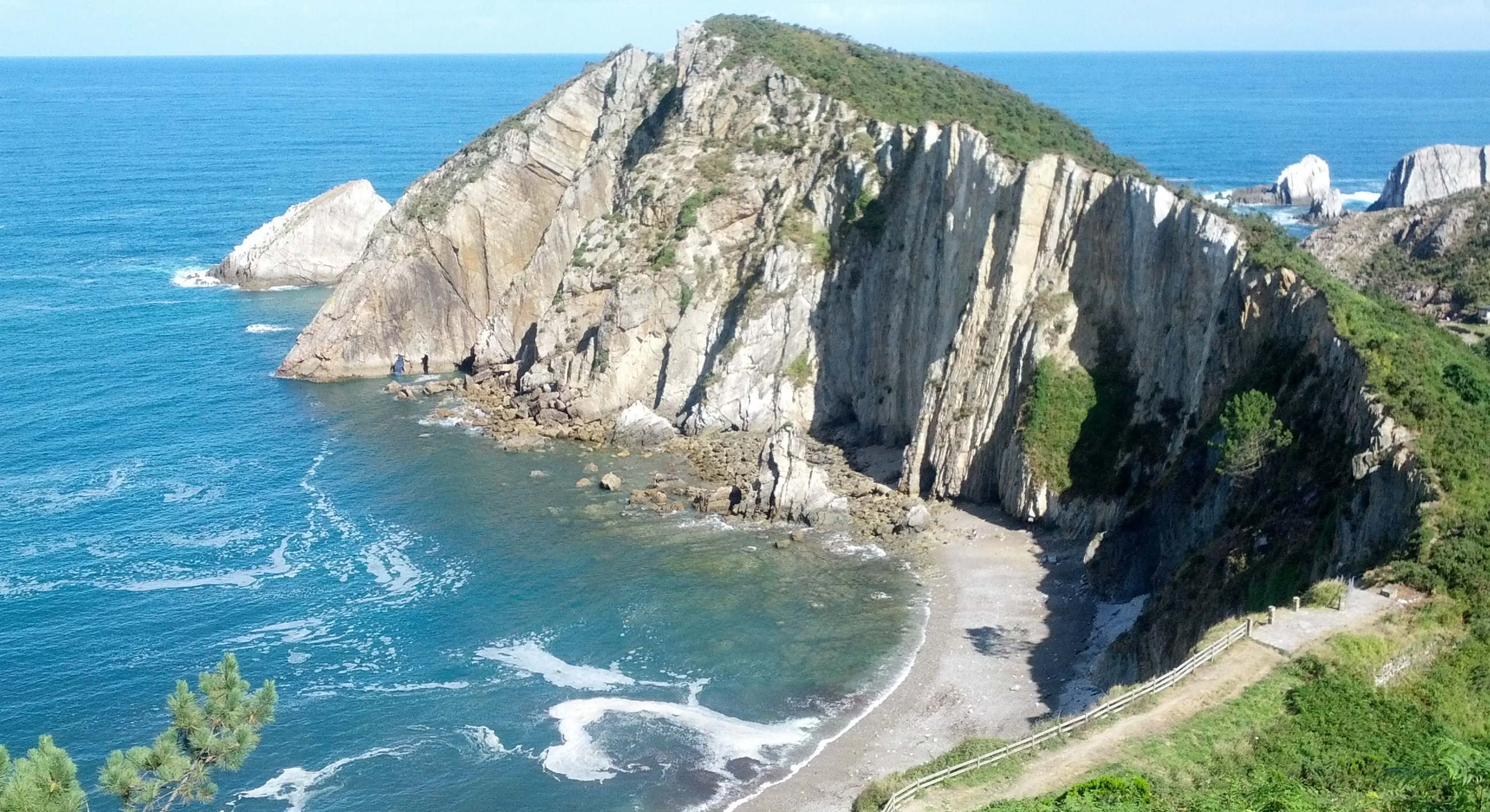 Cala del silencio con un peñón muy grande y rodeado de acantilados y vegetación
