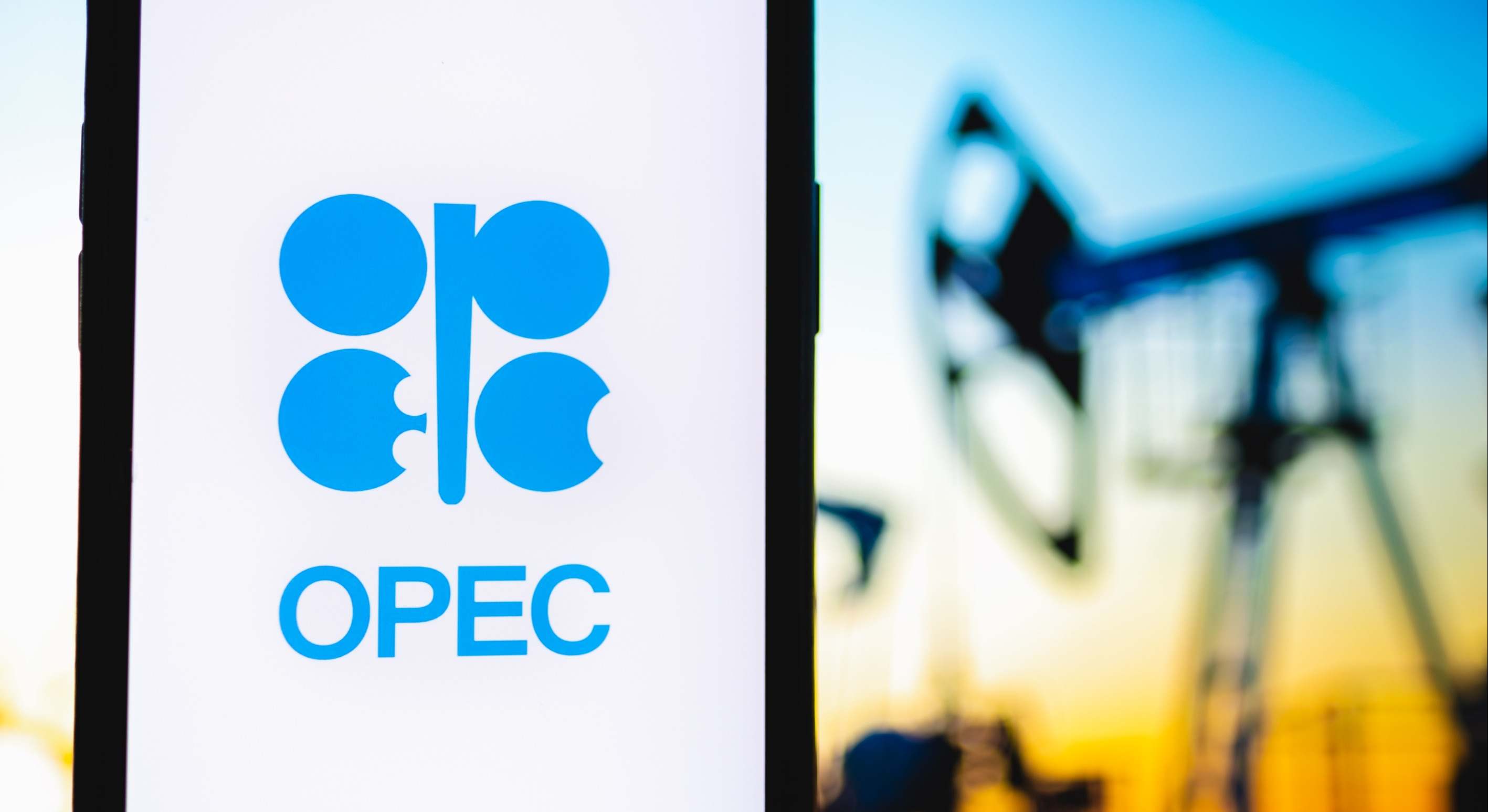 Una pantalla con el logo de la OPEP y de fondo un pozo petrolífero