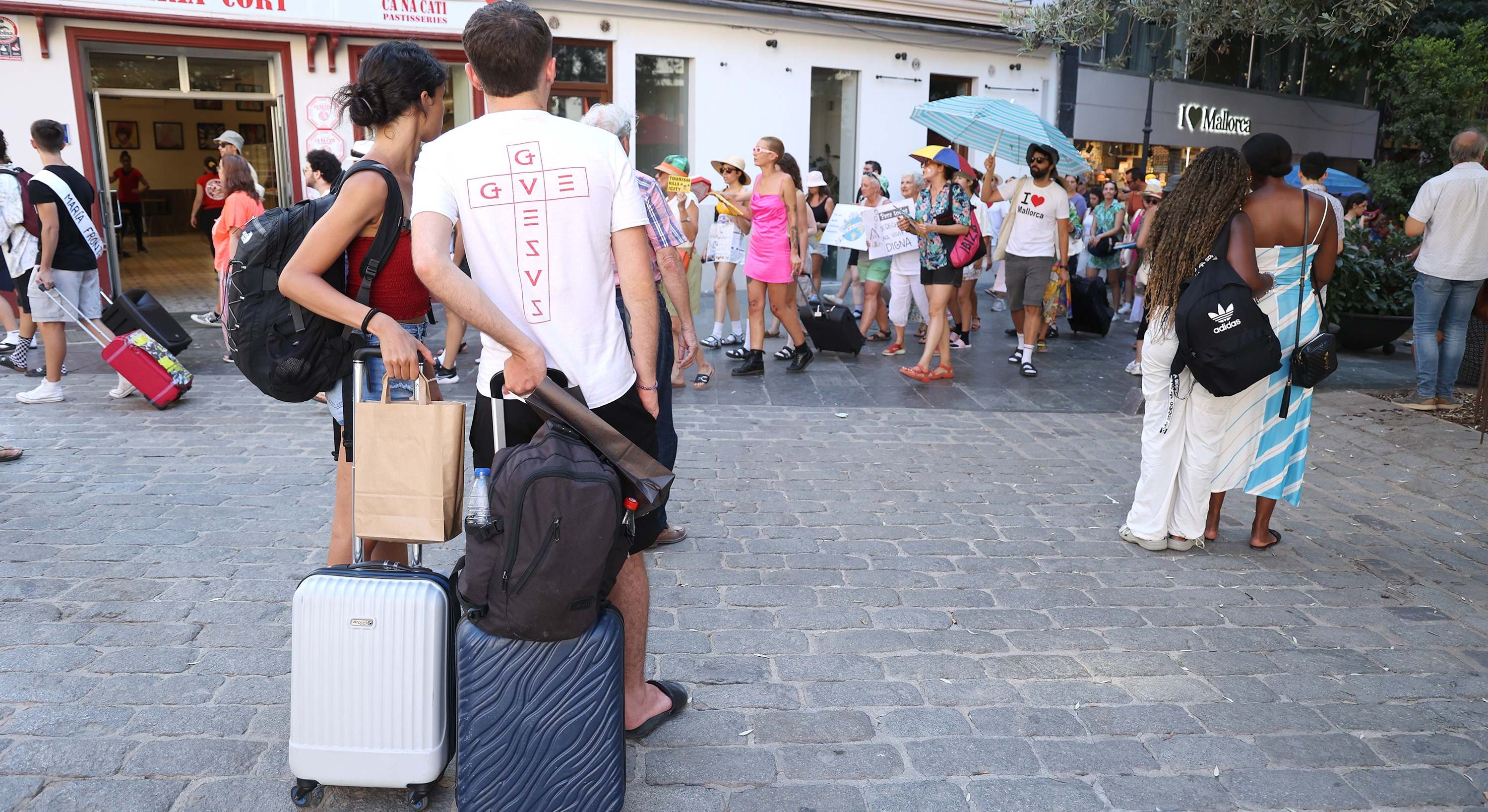 Una manifestación contra el turismo masivo en Mallorca y varios visitantes observando 