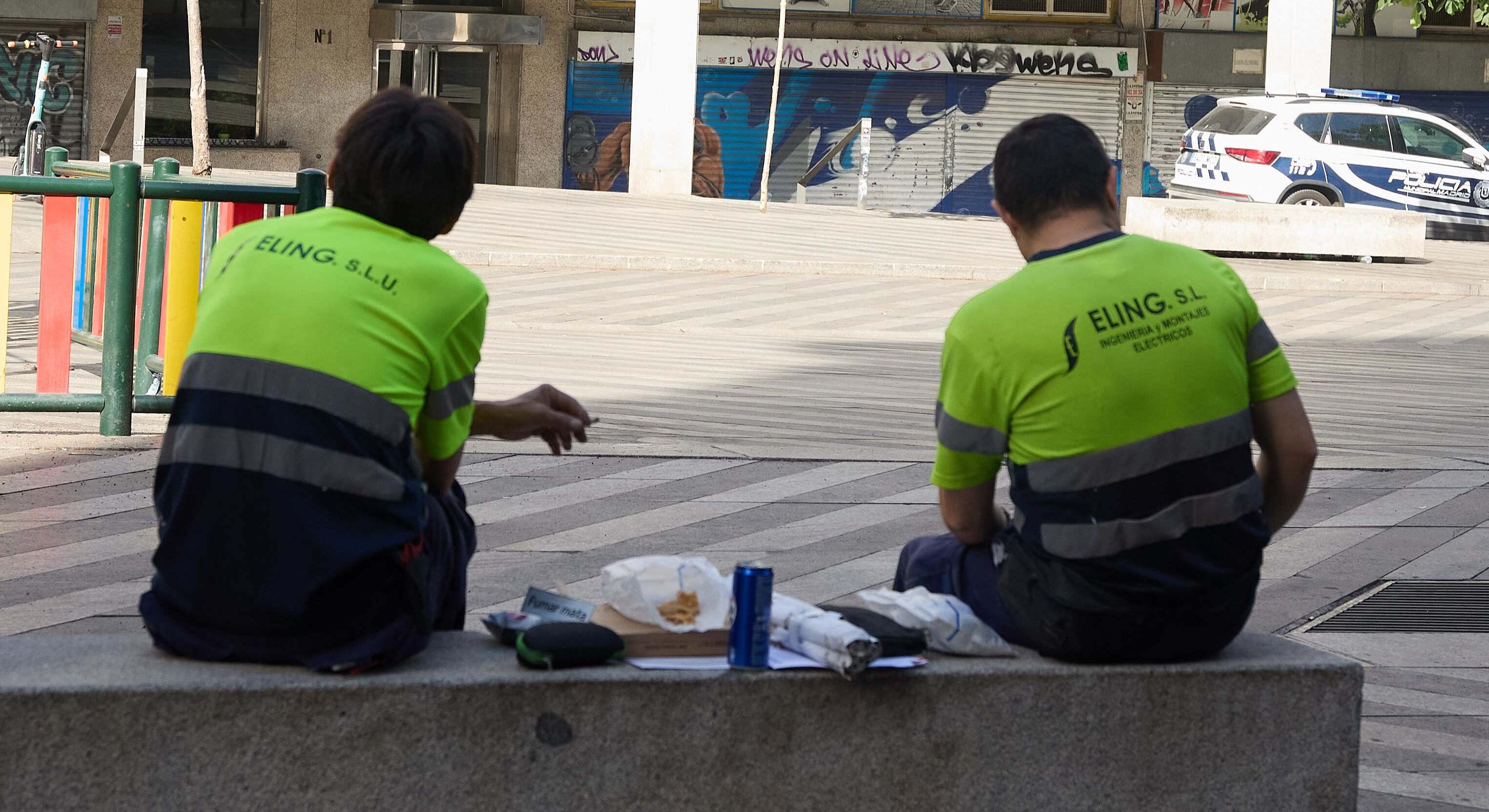 Dos trabajadores al aire libre en una plaza, haciendo un descanso.