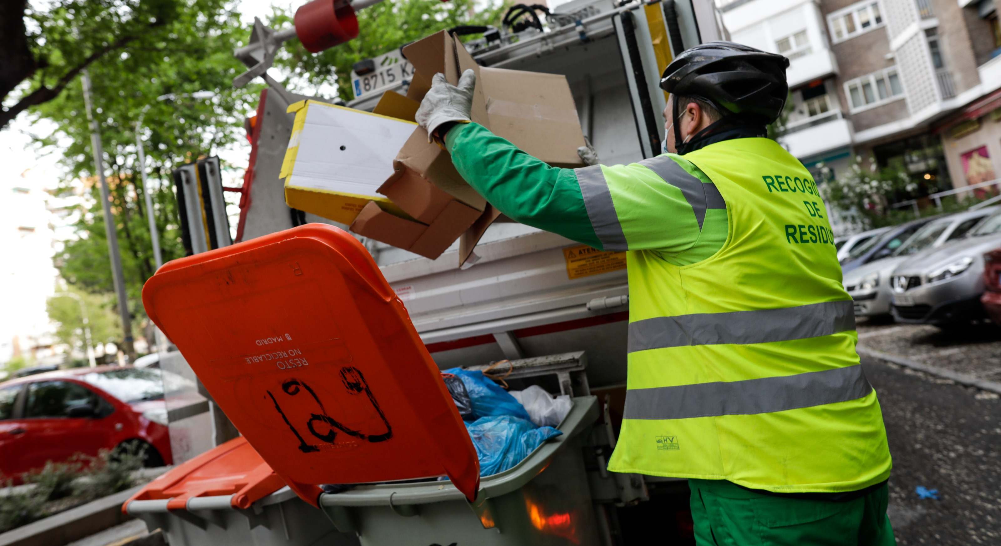 Un operario de recogida de residuos extrae cajas de cartón de un cubo de basura