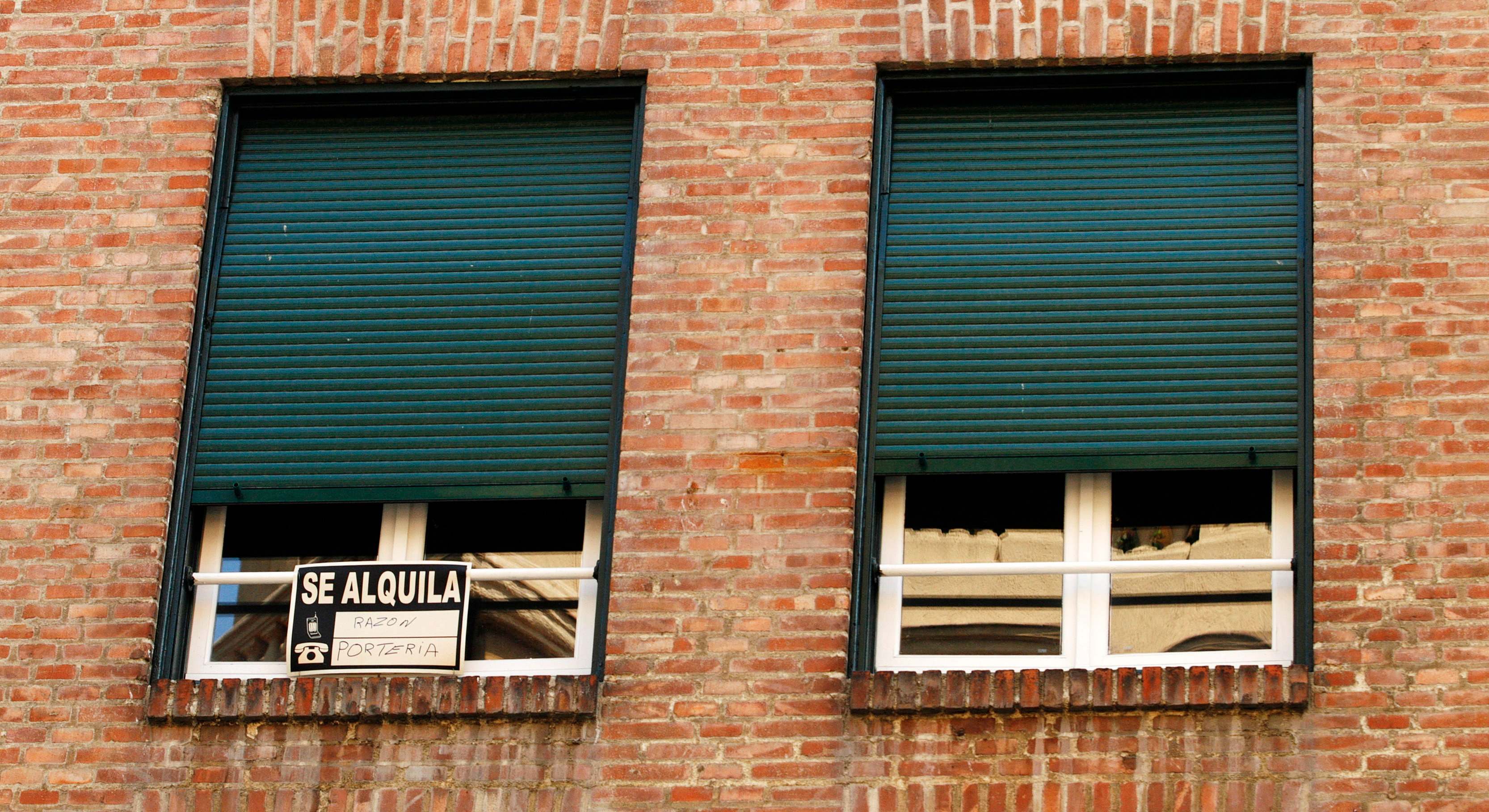 Vista de unas ventanas con un cartel de 'se alquila'.