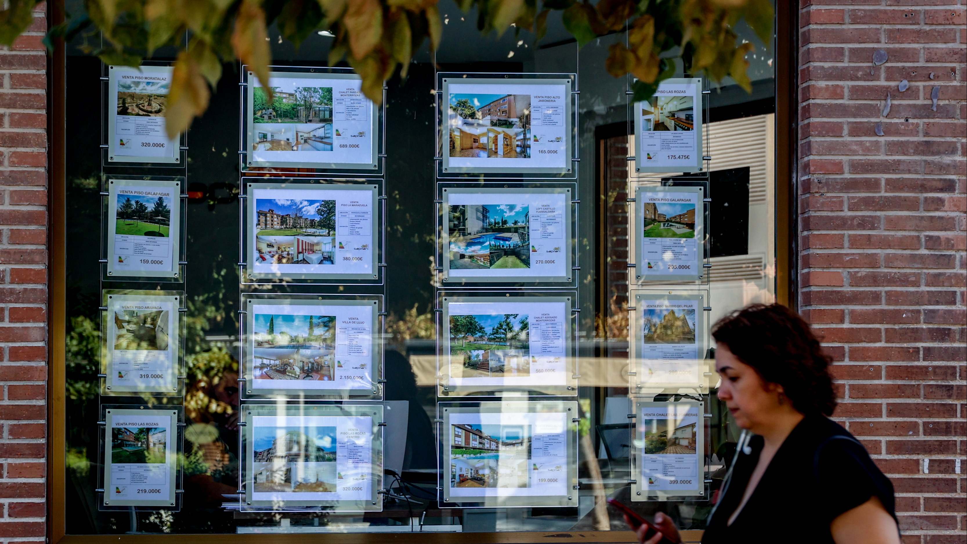 Mujer pasando por delante de una agencia inmobiliaria con anuncios de viviendas en el escaparate. Foto: EP