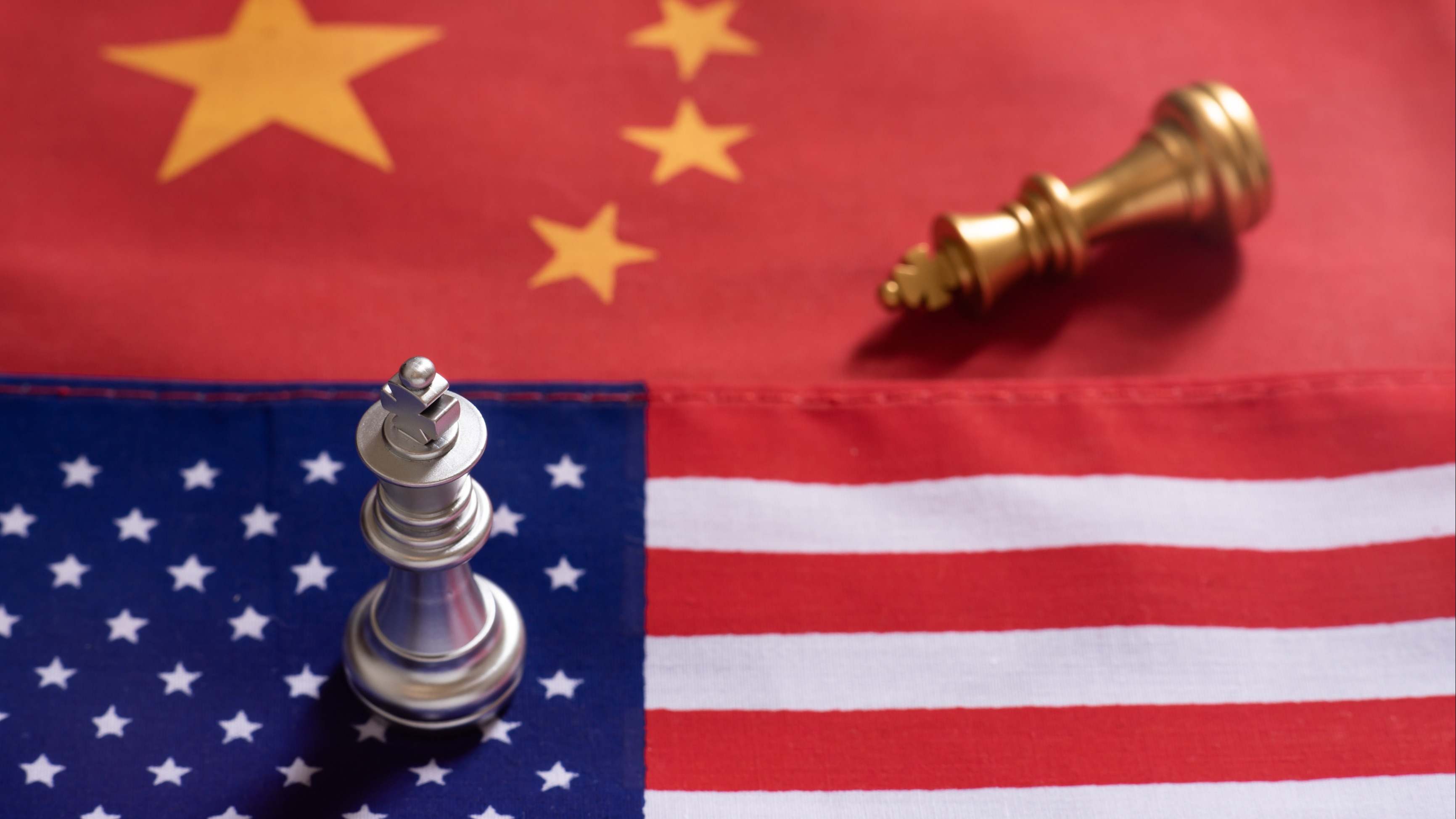 Una ficha de ajedrez caída, sobre una bandera china, frente a una victoriosa sobre una bandera americana