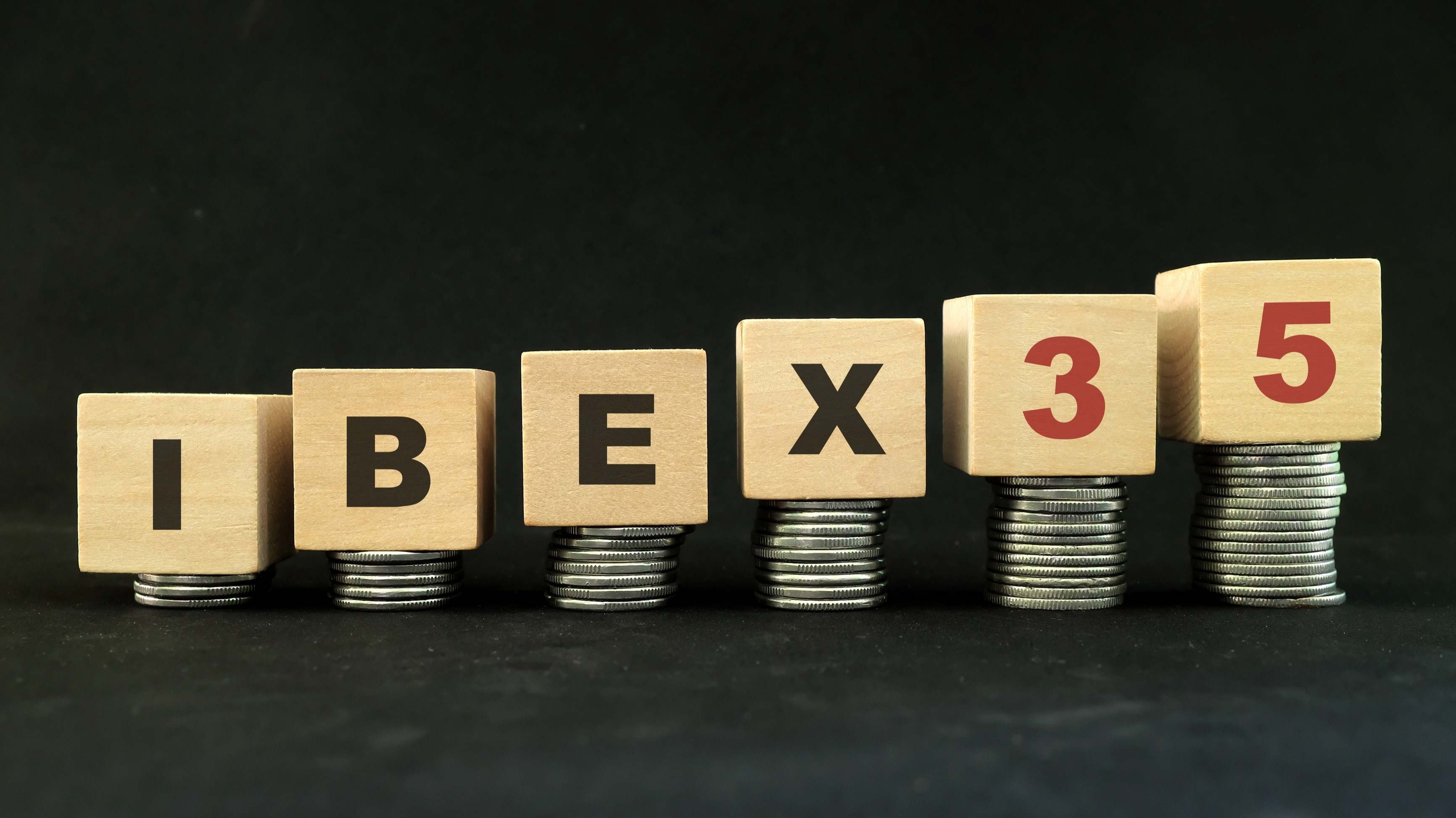 La palabra Ibex 35 se sostiene sobre montones de dinero.