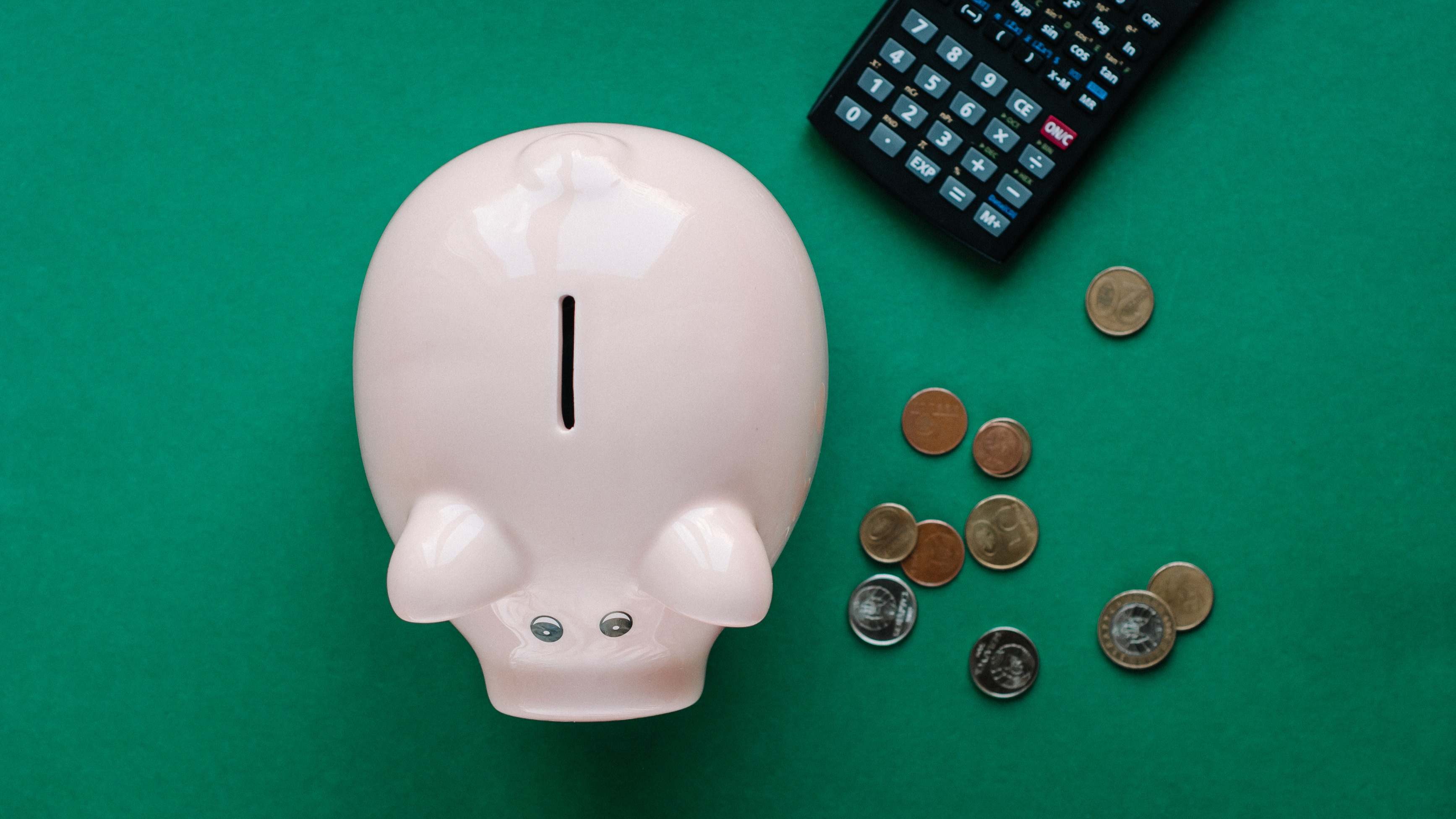 Hucha en forma de cerdito, al lado de unas monedas y una calculadora