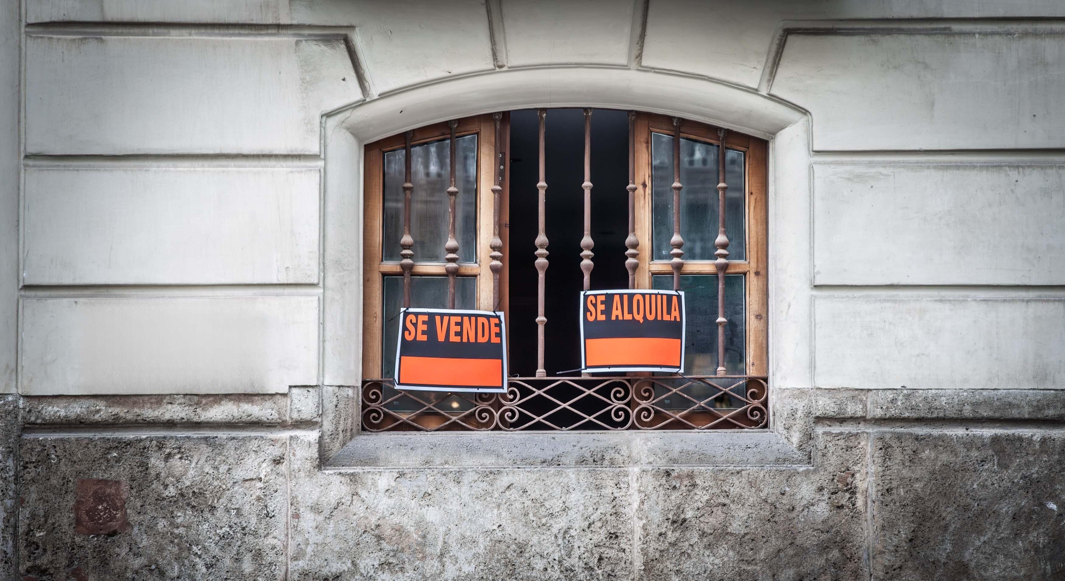 Una ventana con dos carteles, uno de alquiler y otro de venta