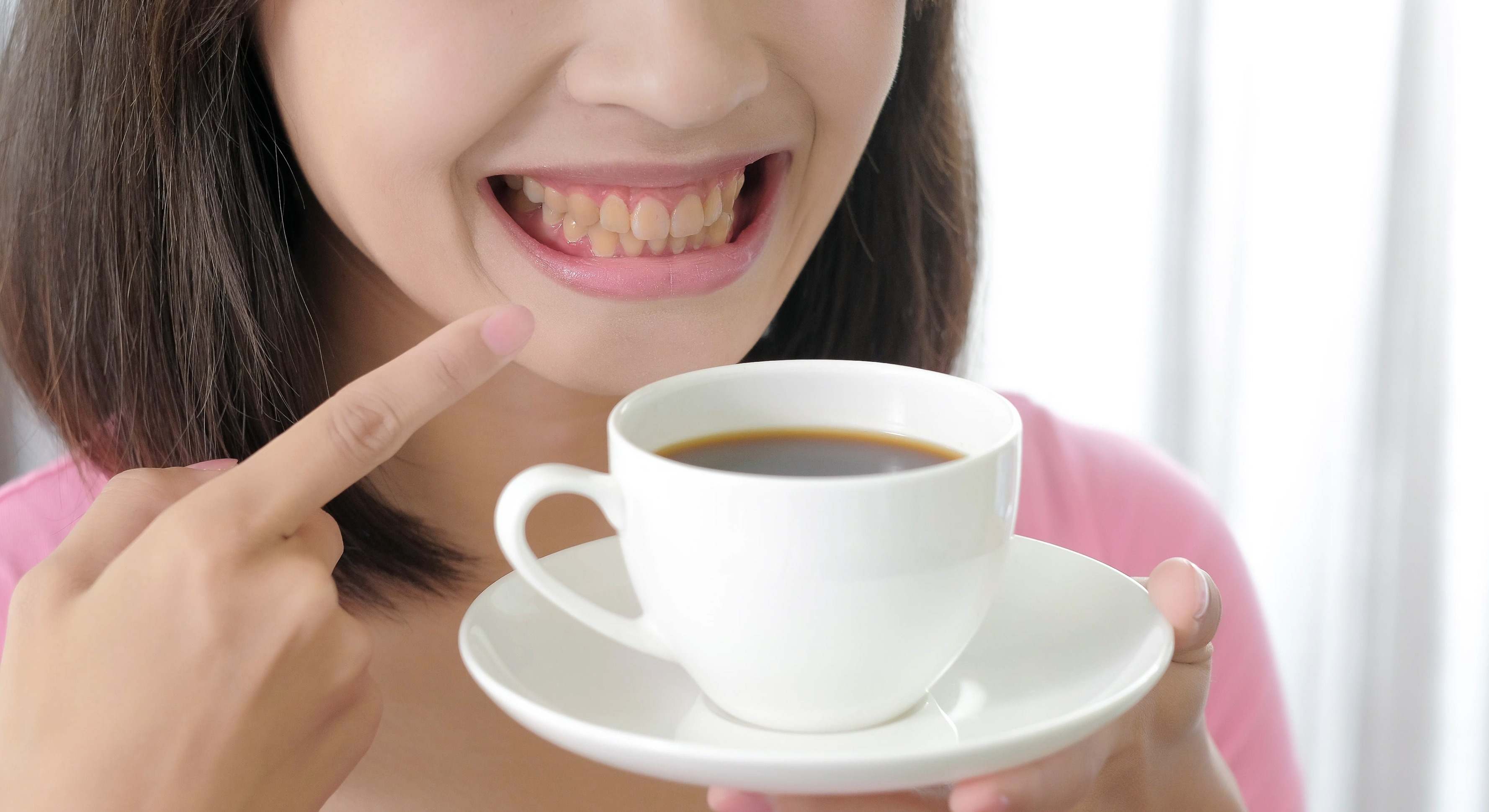 Mujer sujetando un café mientras se señala los dientes