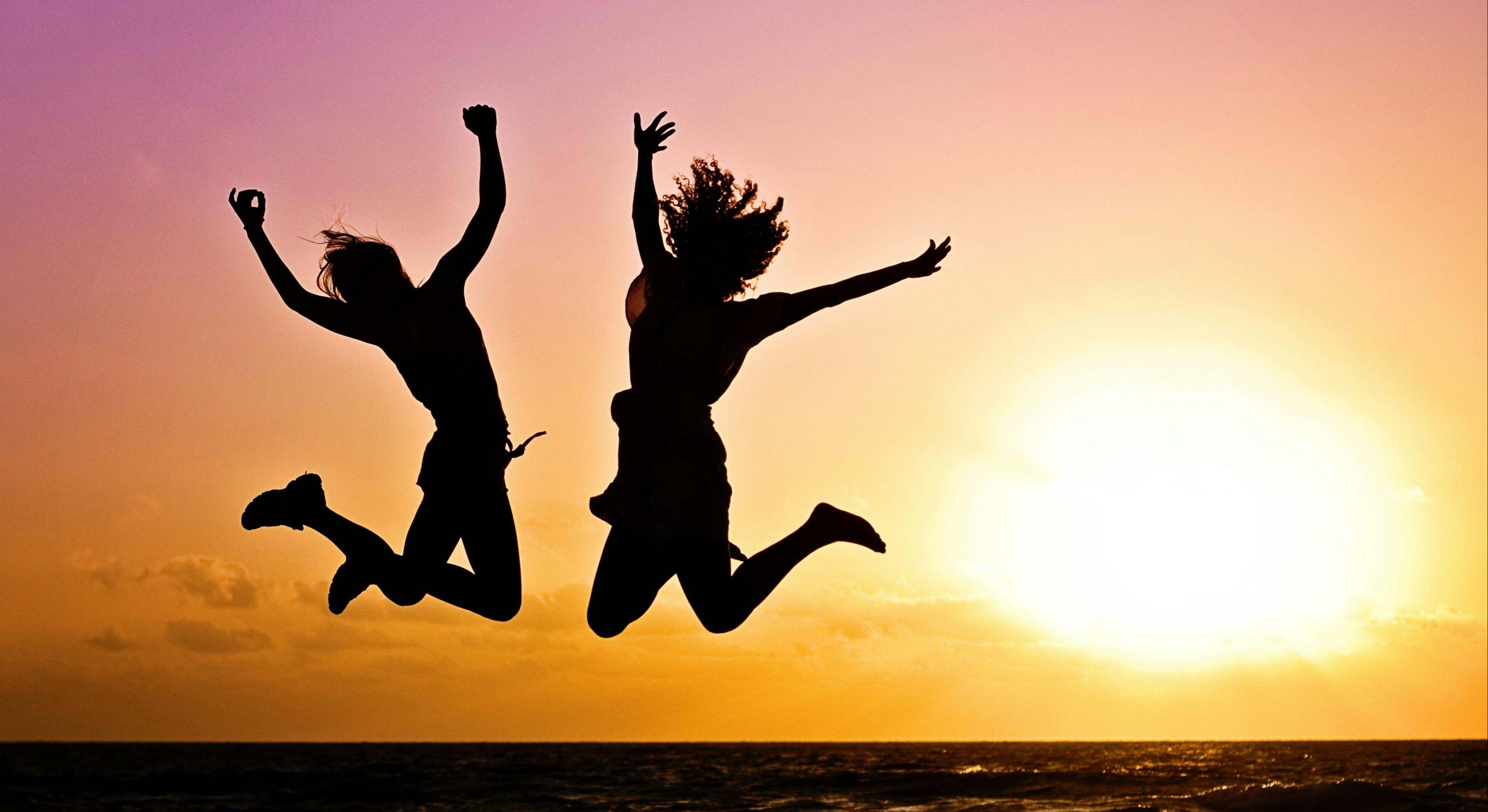 Dos personas con más de 40 años saltan felices con una puesta de sol de fondo