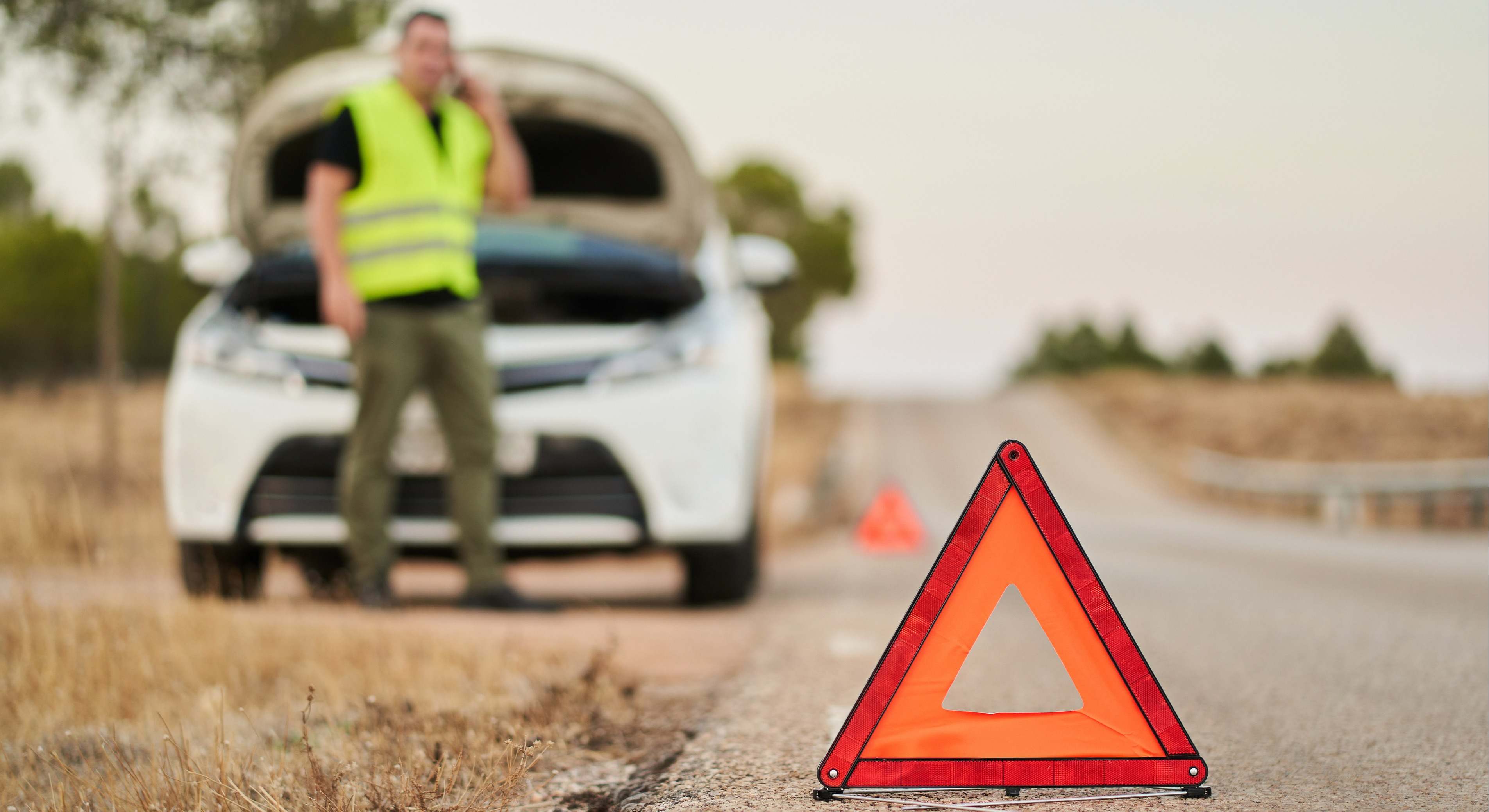 Triángulos de emergencia que señalan una avería en el automóvil y un hombre que llama al seguro del automóvil para obtener ayuda