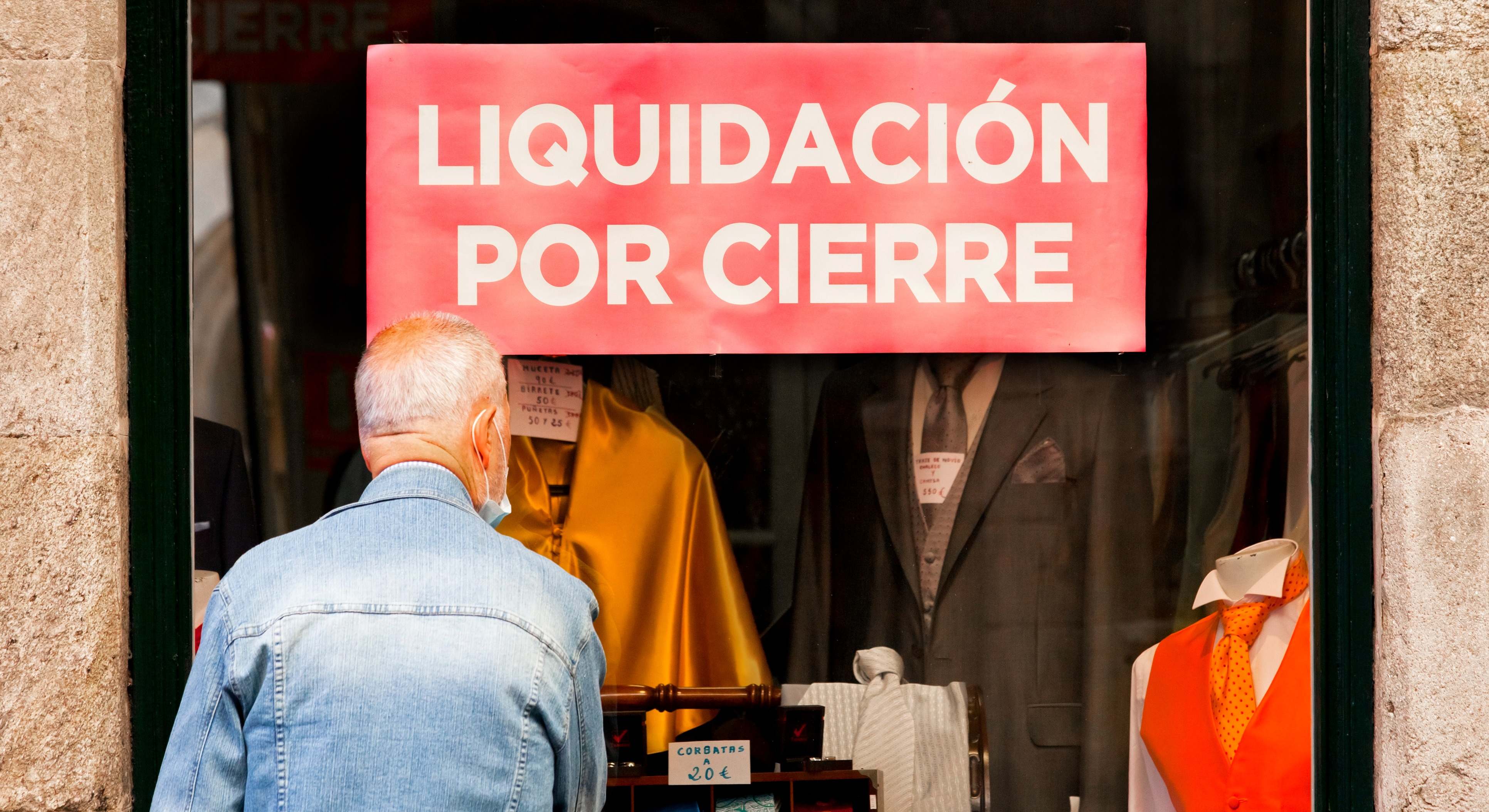 Una persona mira el escaparate de un negocio en liquidación por cierre