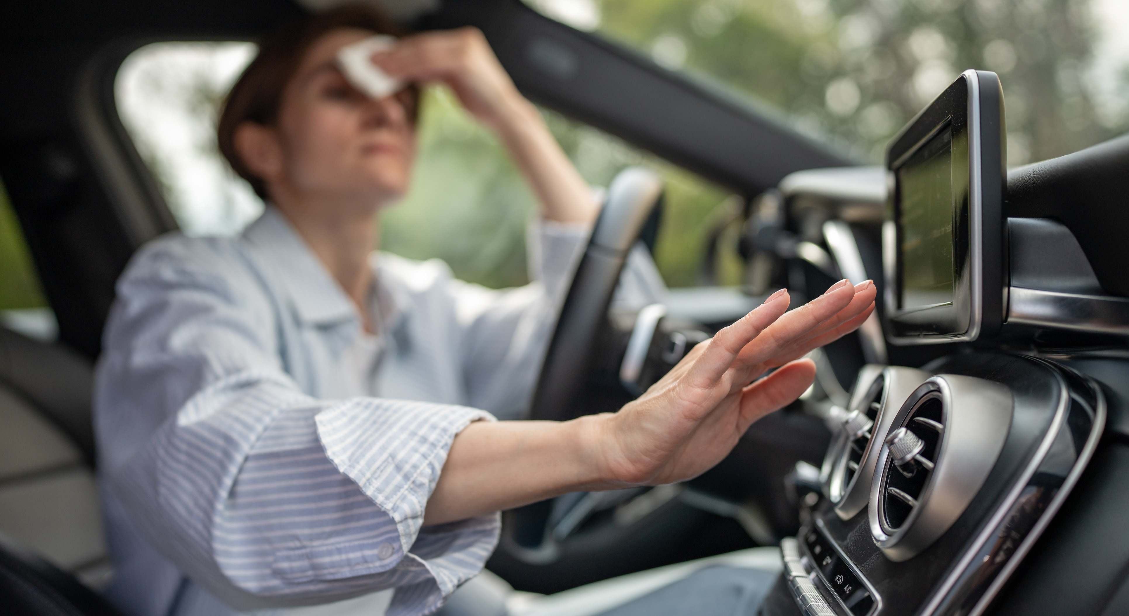 Mujer en el coche comprobando la potencia del aire acondicionado en plena ola de calor