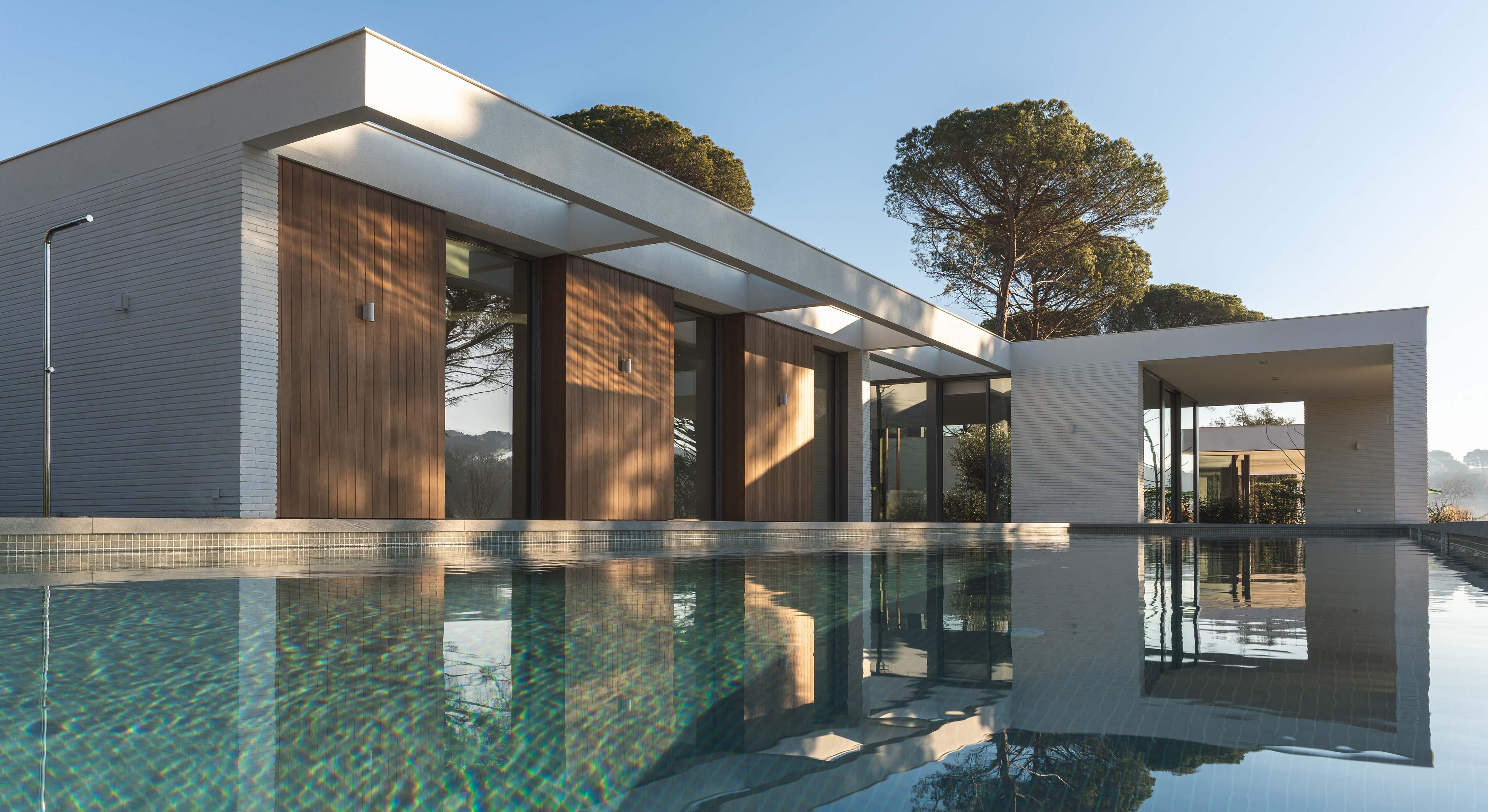 Casa moderna blanca y de madera con piscina y pinos en el exterior