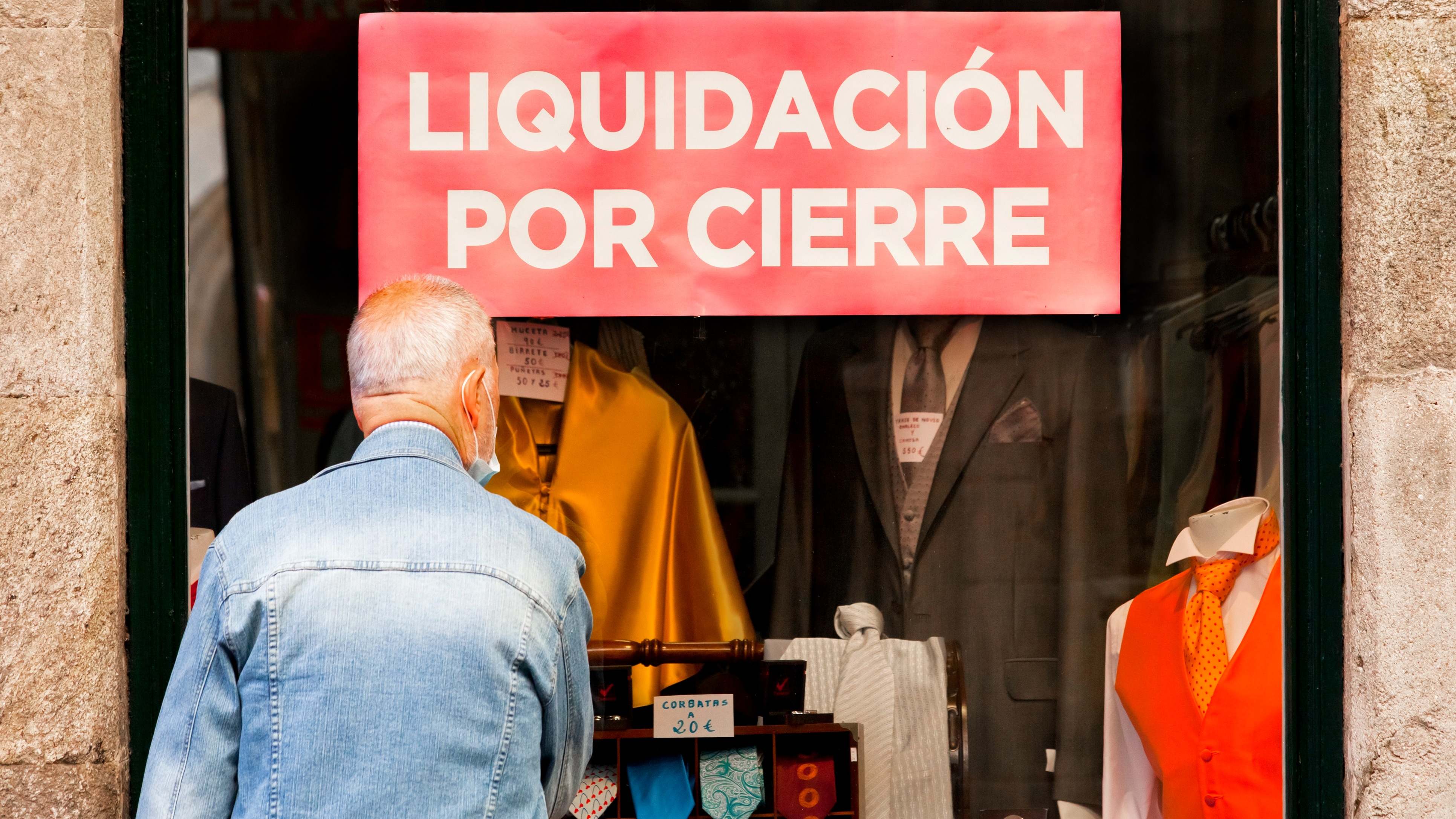 Un hombre mira el escaparate de un negocio en liquidación por cierre