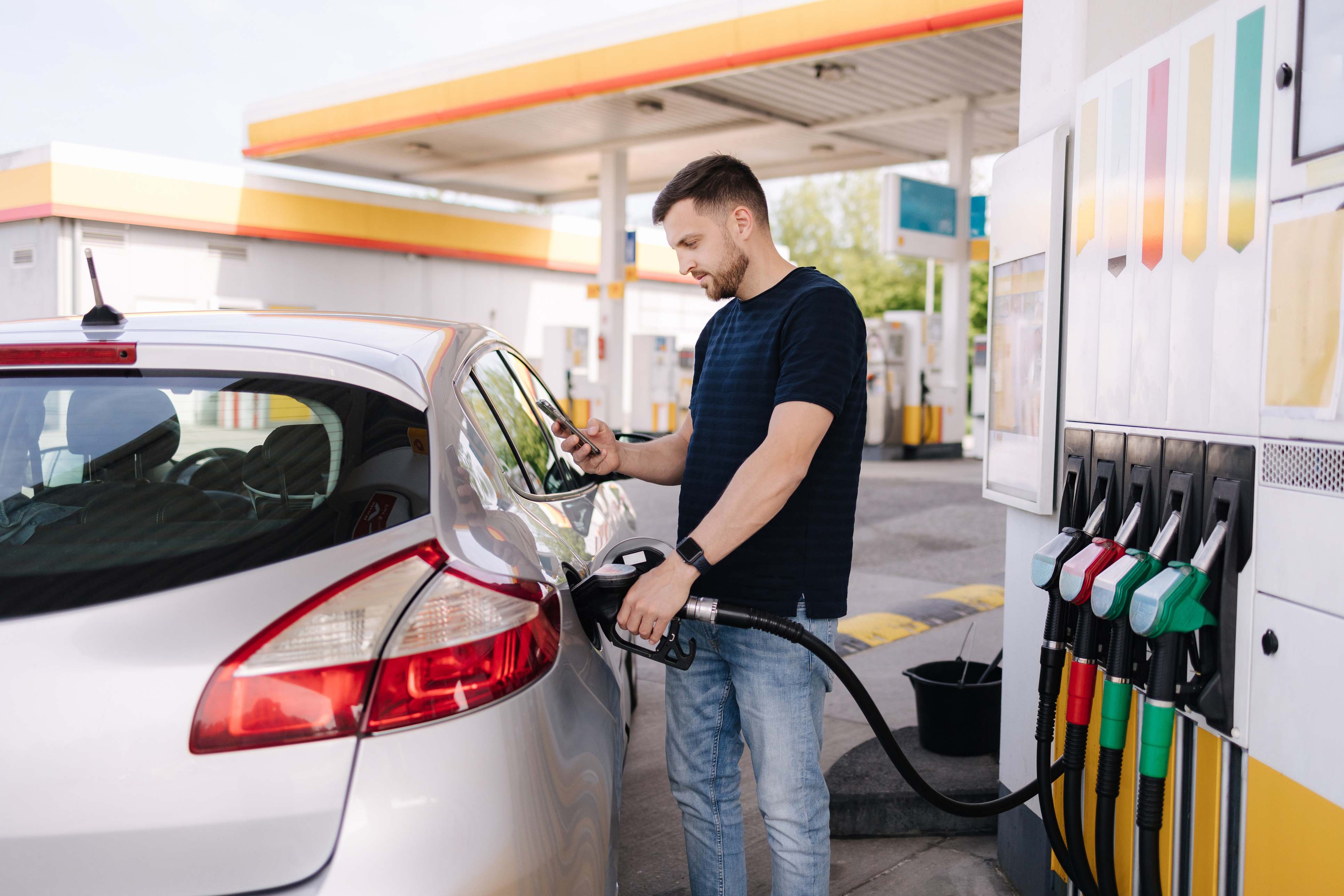 Hombre echando gasolina en una gasolinera mientras mira su teléfono