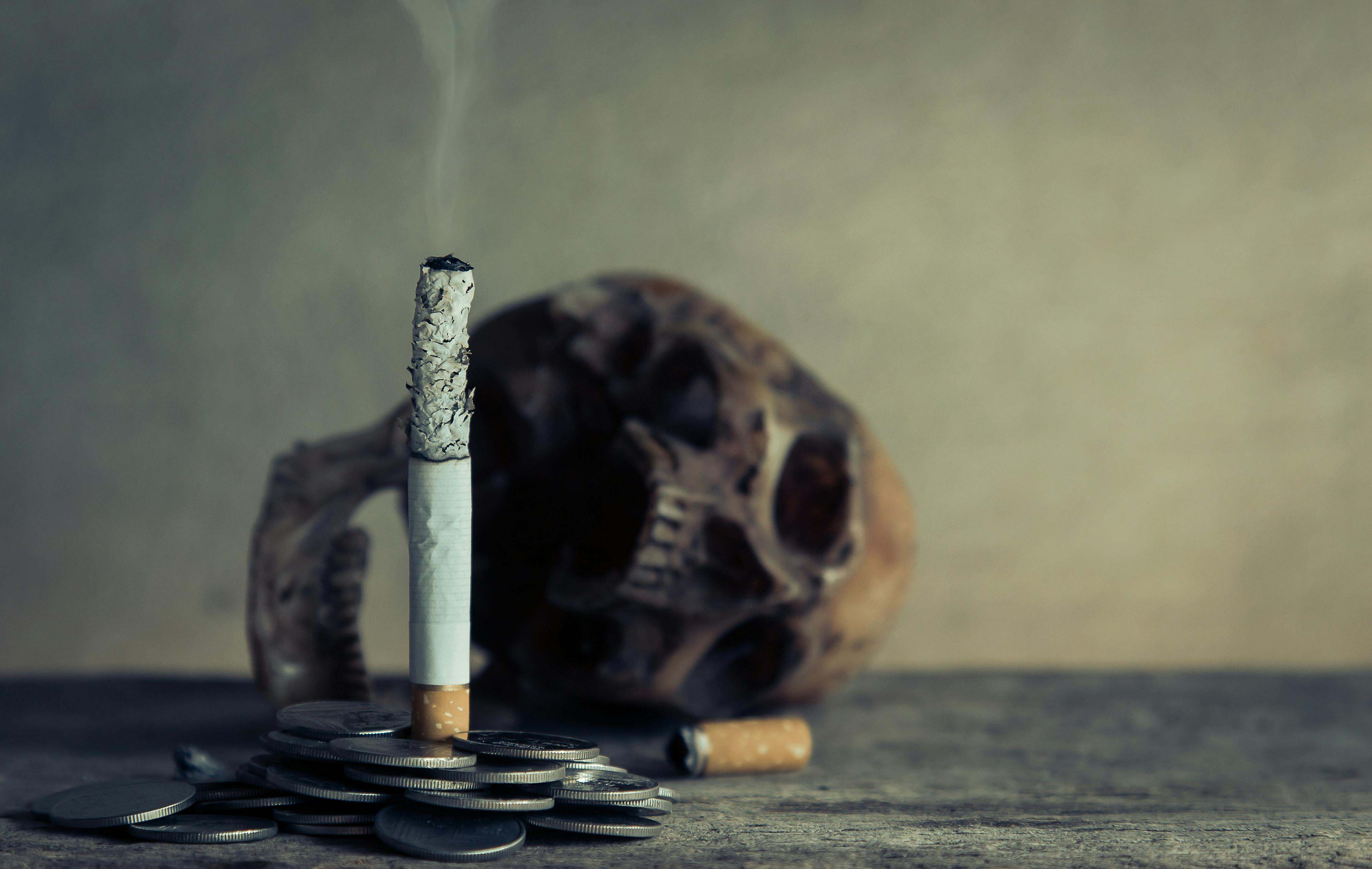 Un cigarrillo encendido con una calavera de fondo