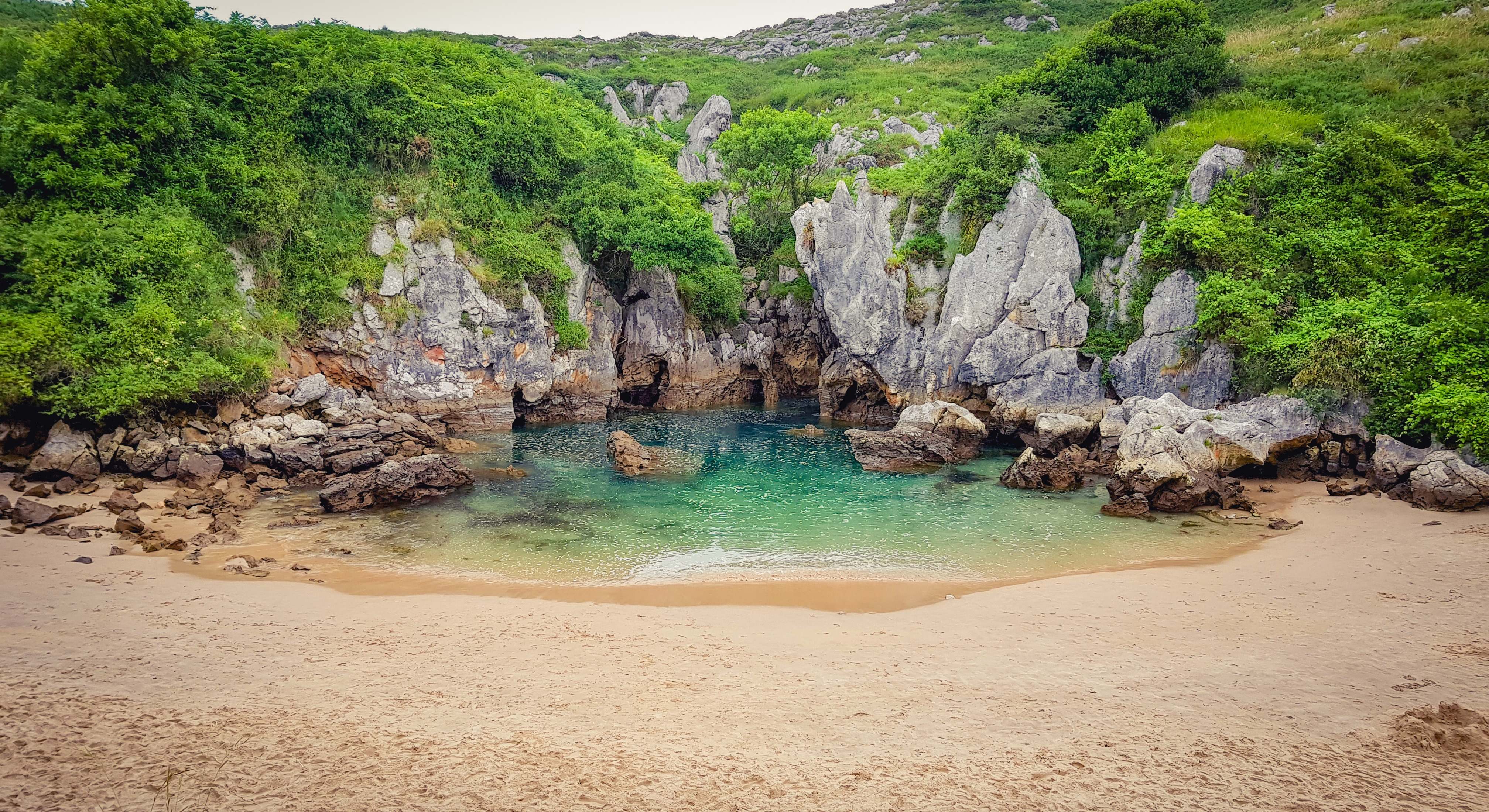 Playa de Gulpiyuri formada por rocas y repleta de vegetación
