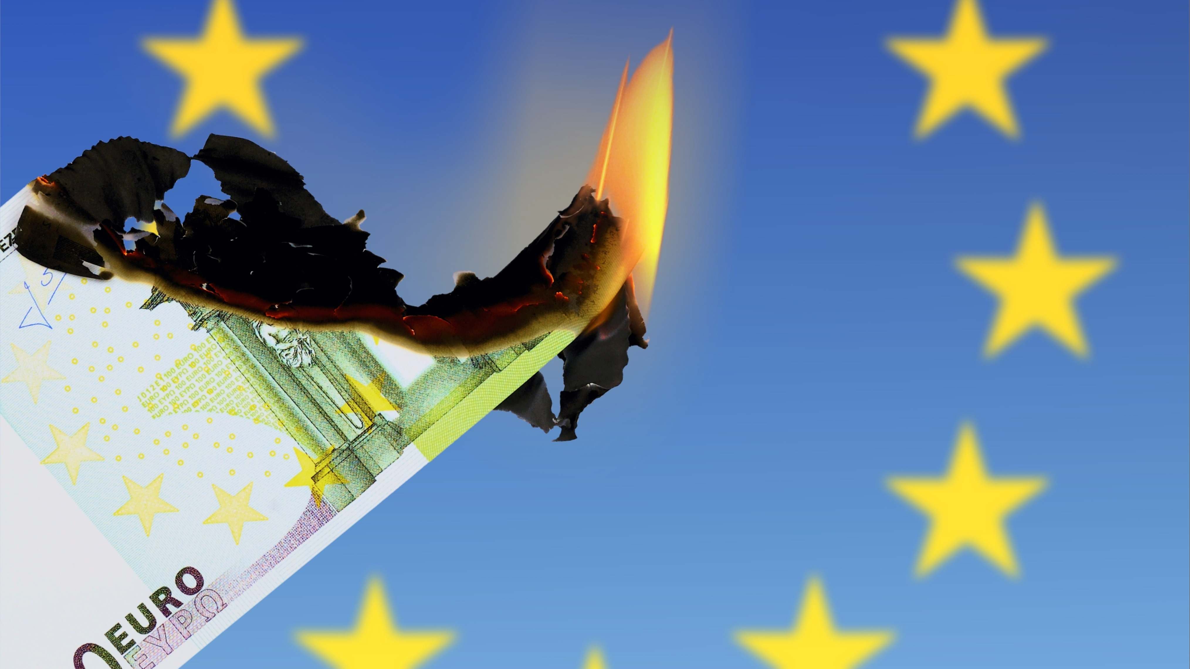 Un billete de 100 euros ardiendo sobre una bandera de la UE