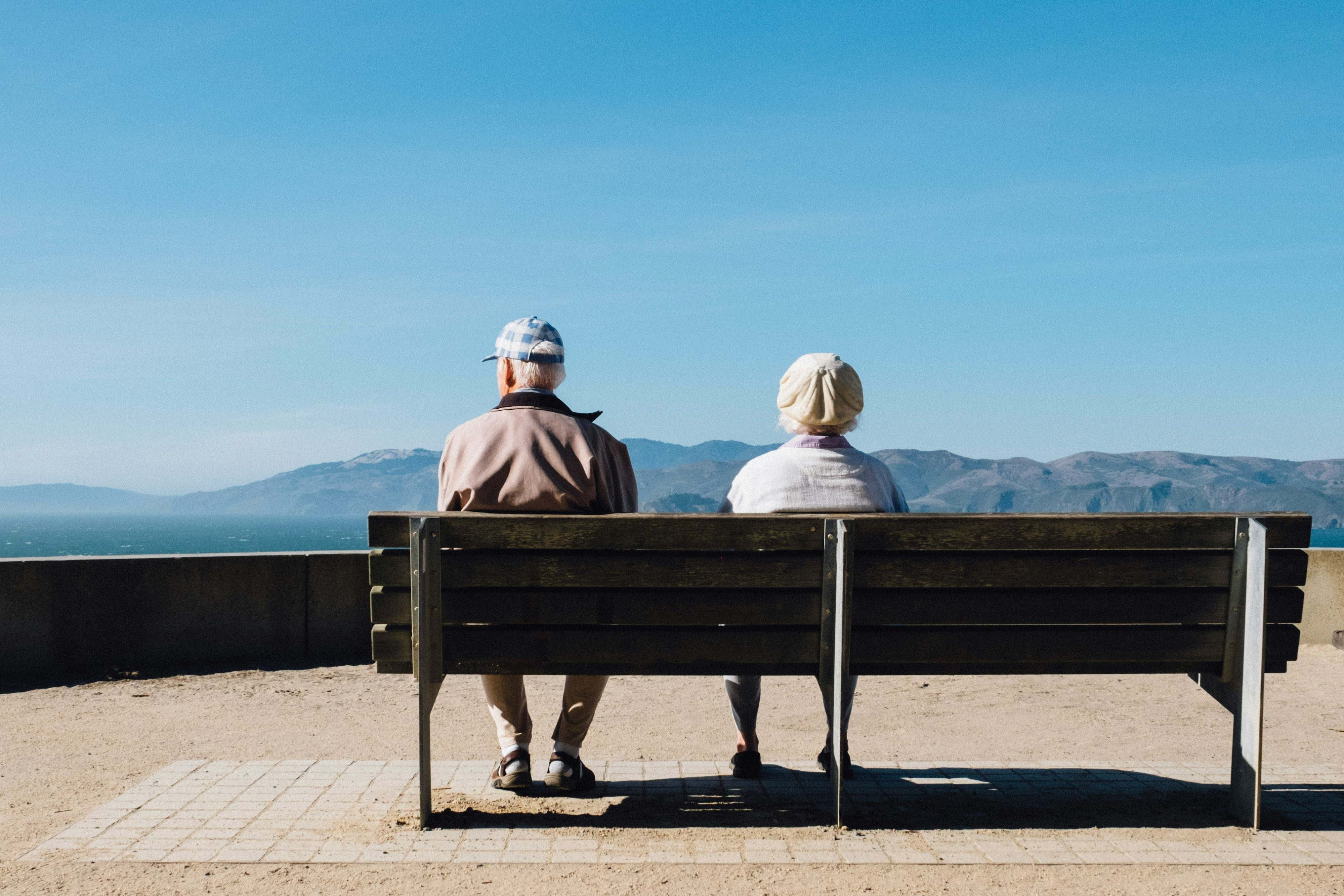 Dos personas de avanzada edad sentadas en un banco miran al mar