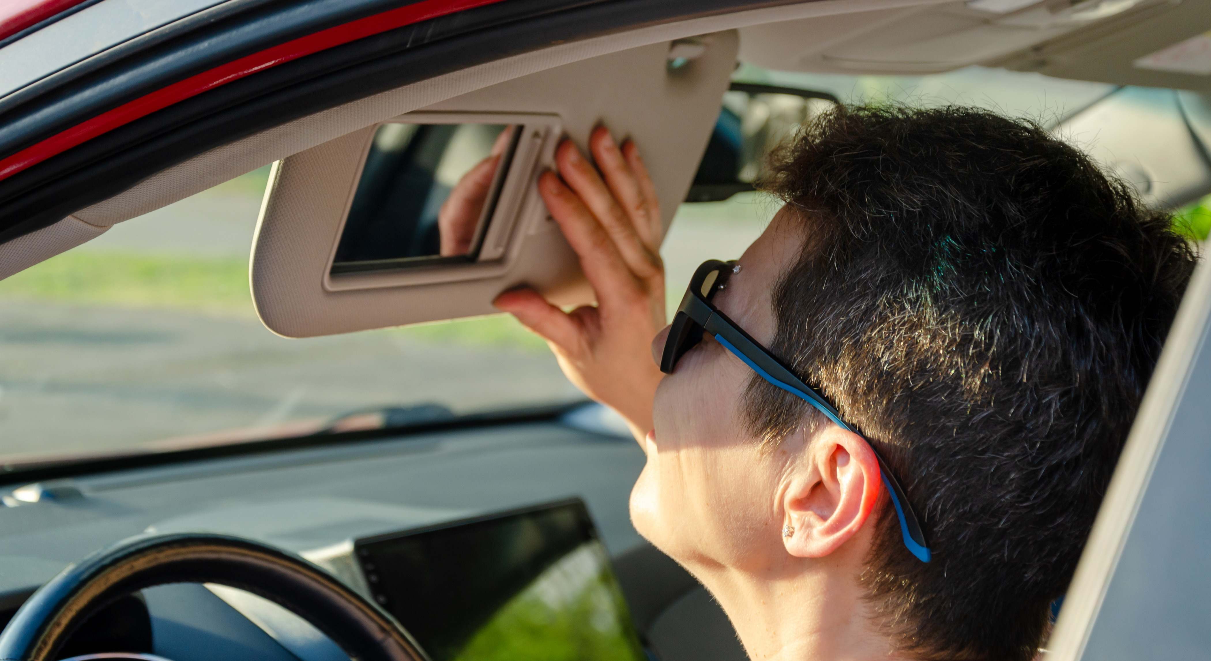  Mujer mira por el retrovisor del coche y ajusta el parasol mientras está sentada en el coche con gafas de sol