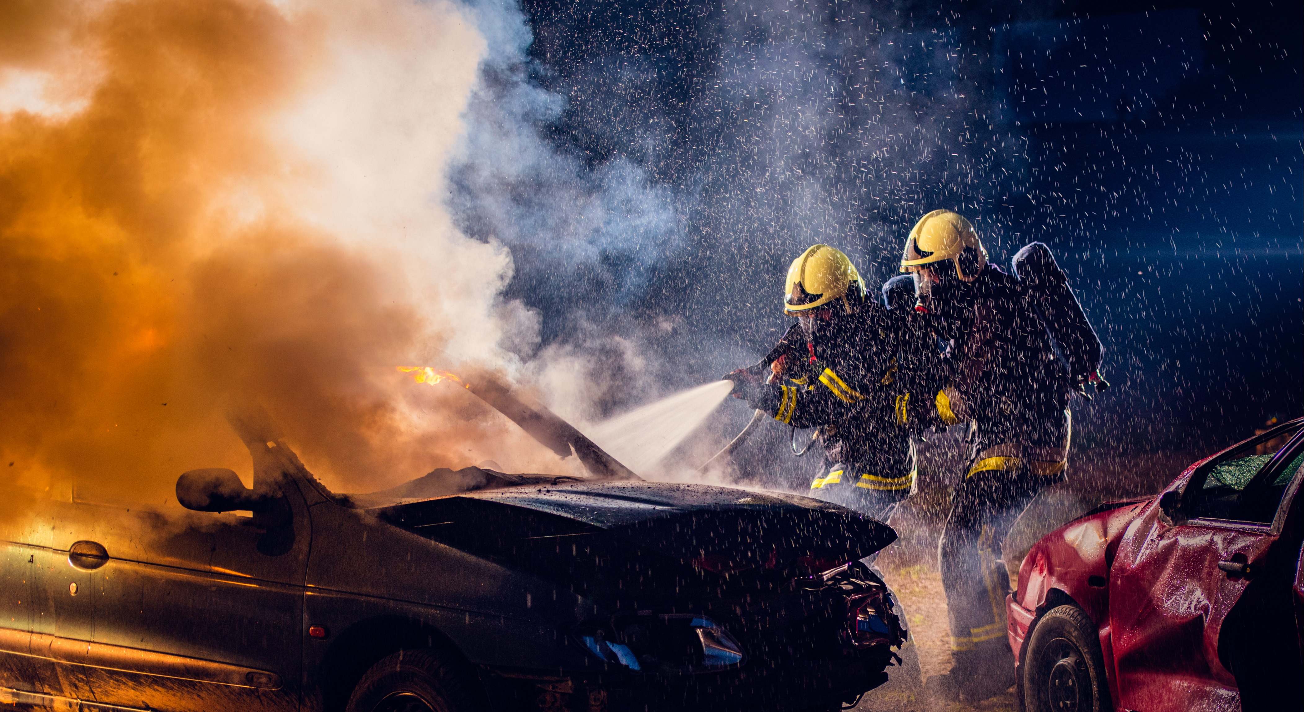 Dos bomberos tratando de extinguir un coche ardiente después de un accidente de tráfico