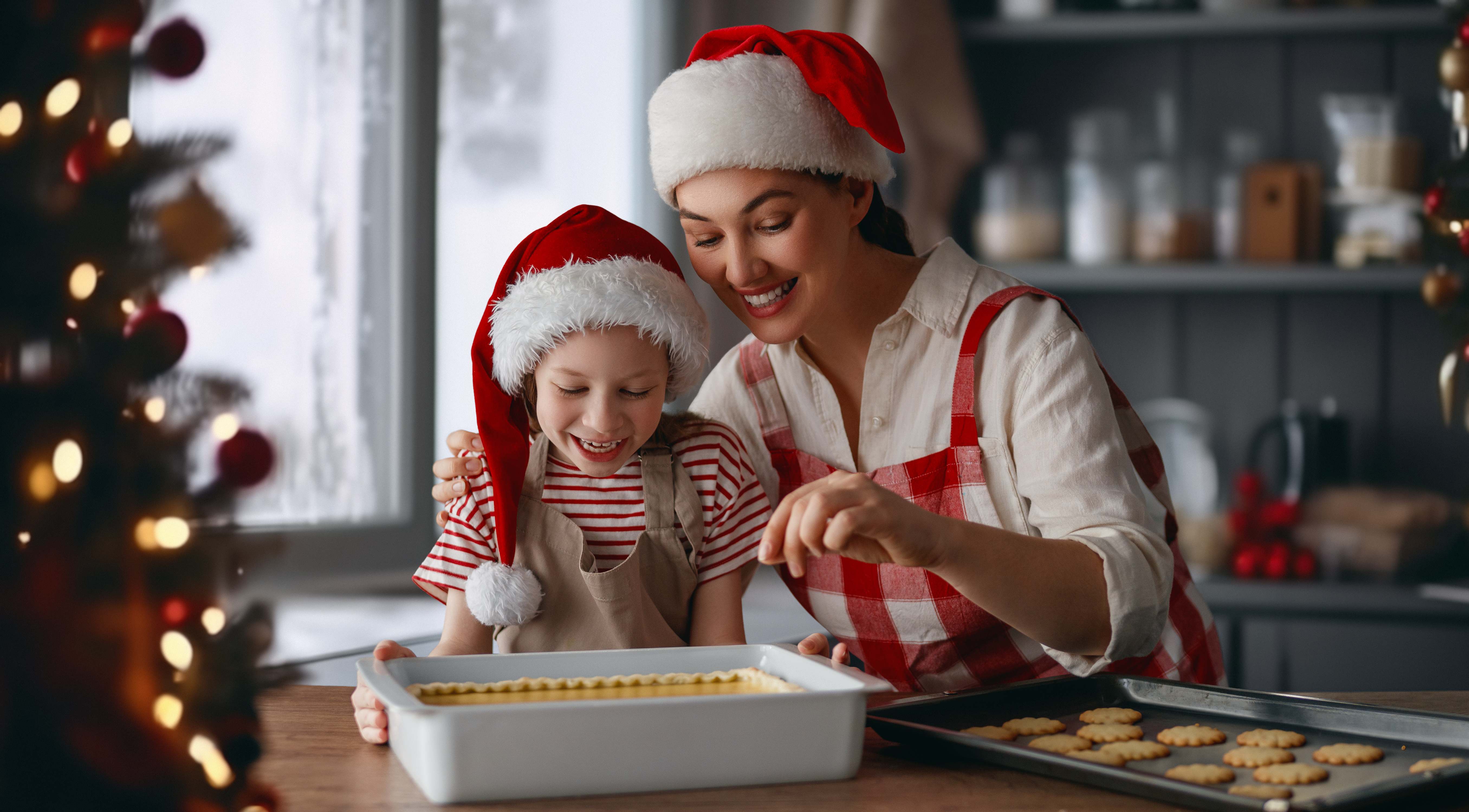 Una madre junto a su hija cocinando con gorros de papá noel