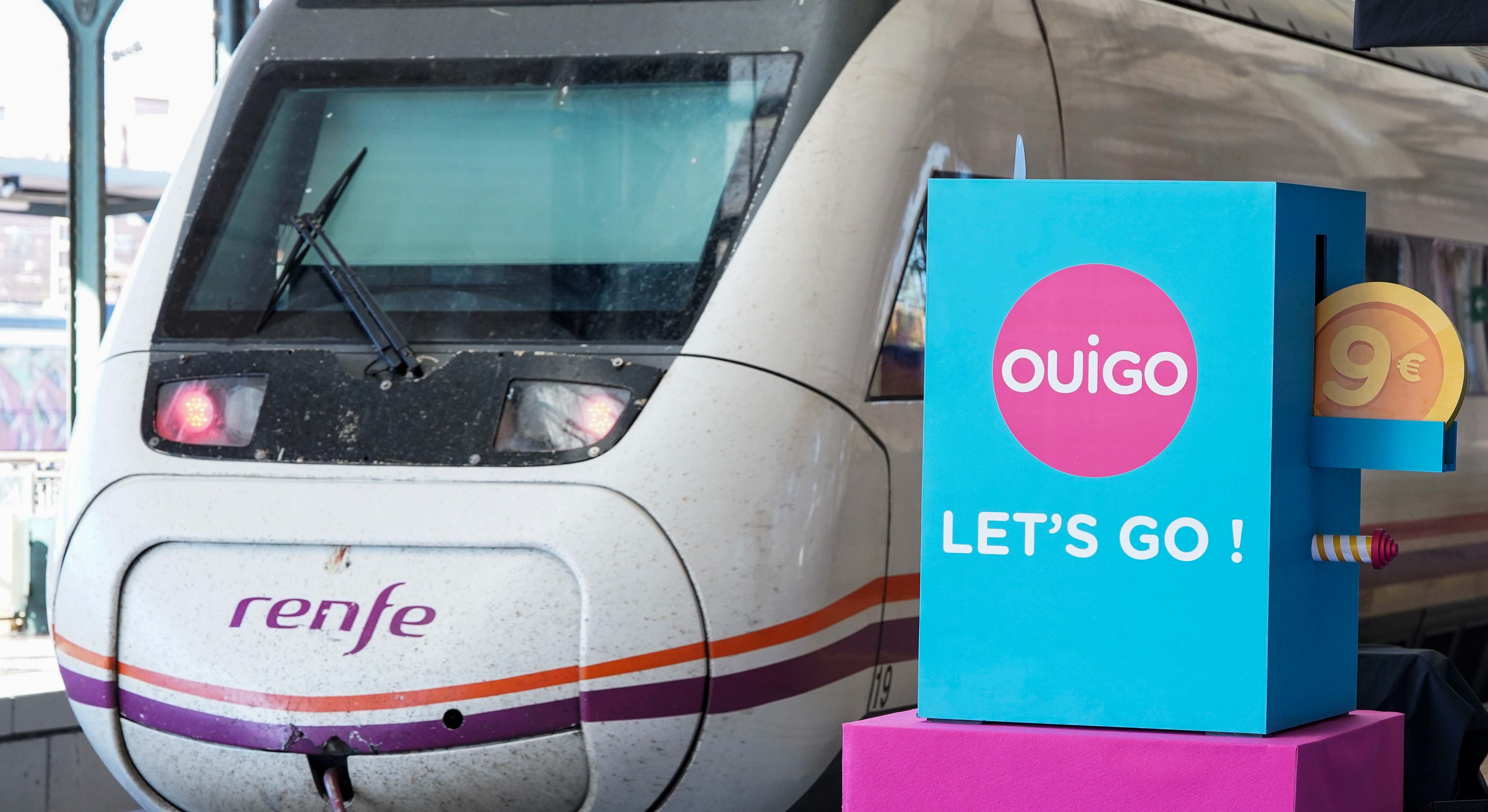 Tren de Renfe circula junto a un cartel publicitario de Ouigo. / EFE