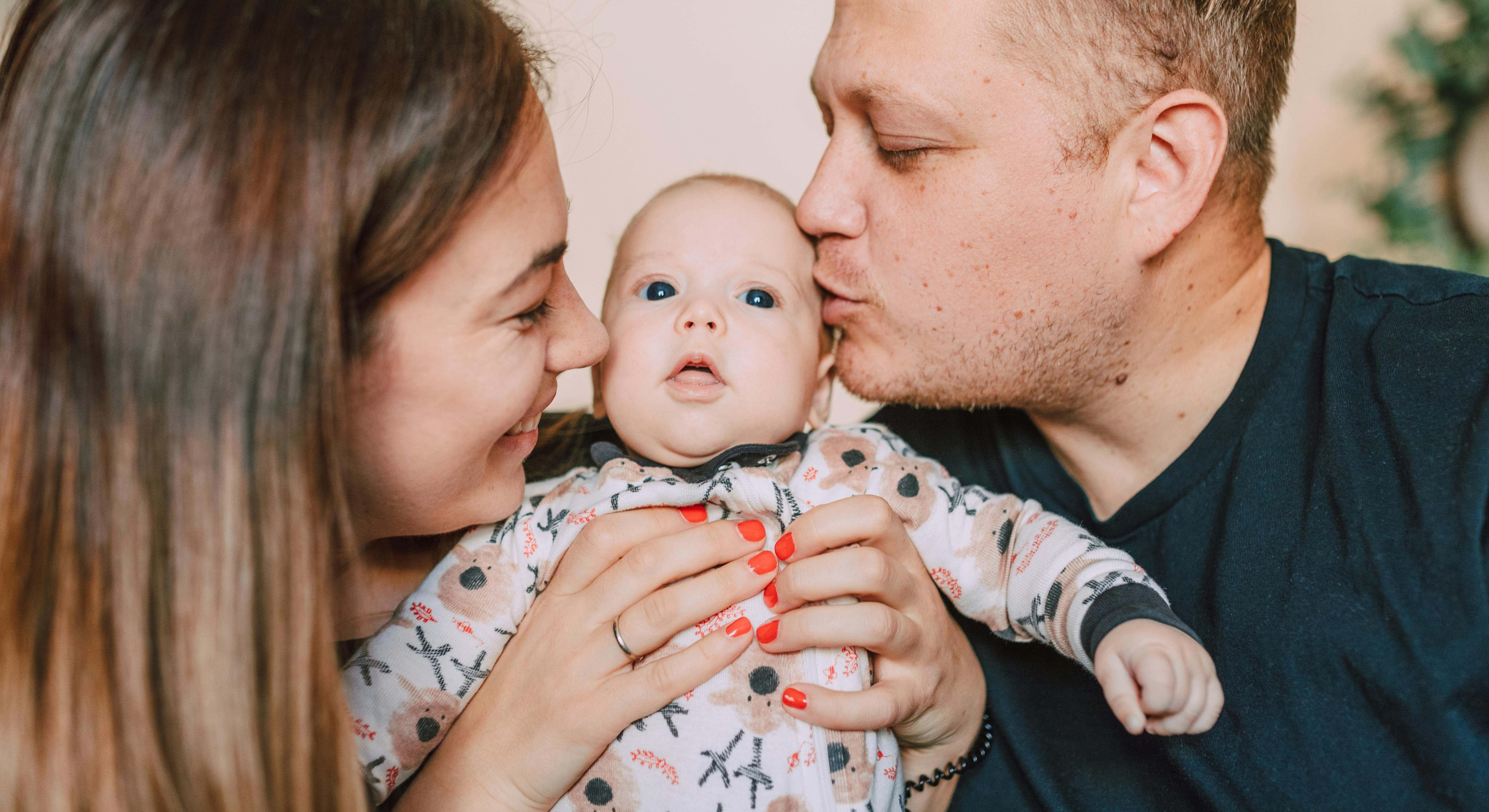Bebé siendo besado por sus dos padres mientras lo cogen en brazos
