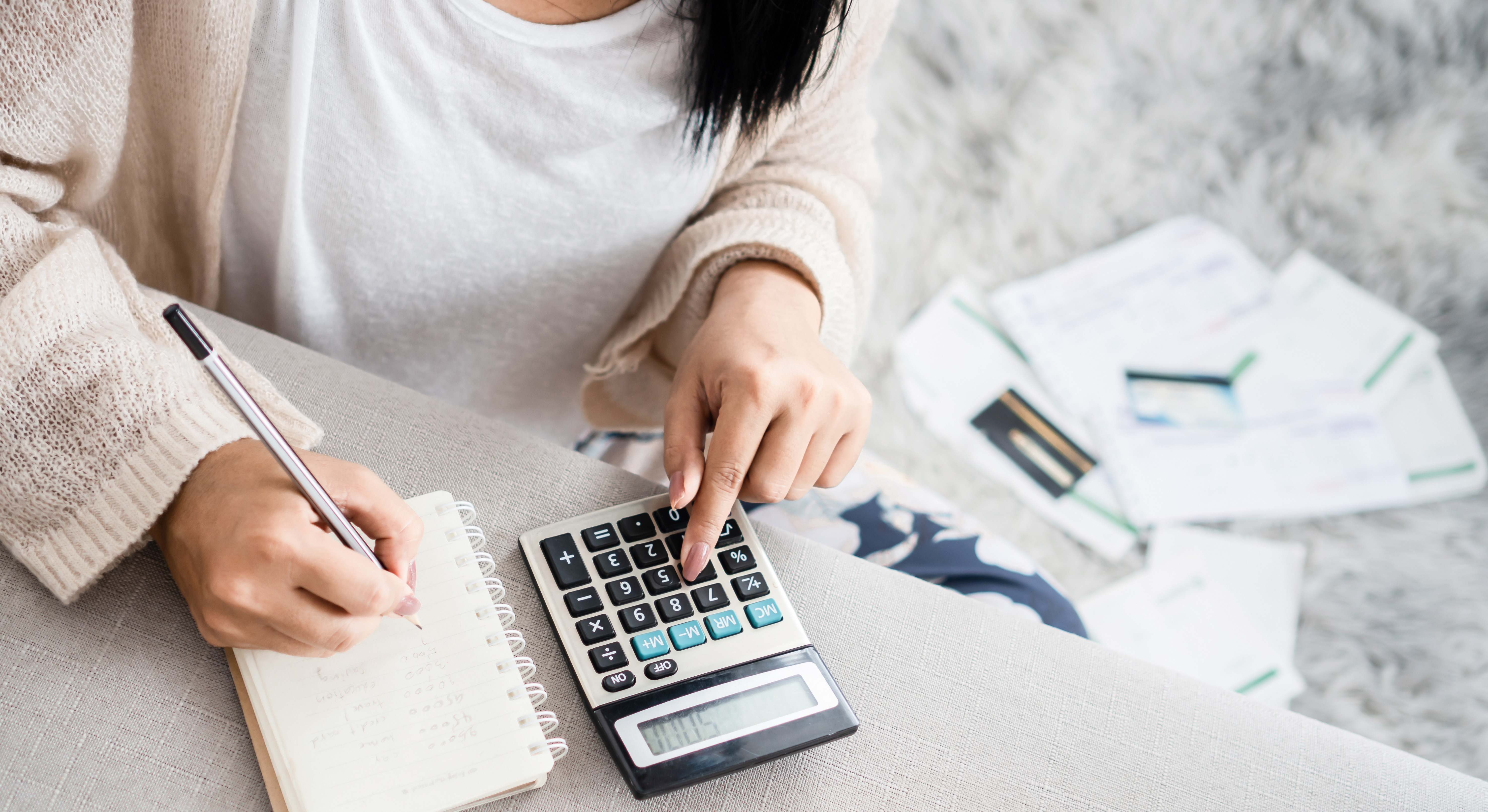 Mujer escribiendo en una libreta con una calculadora