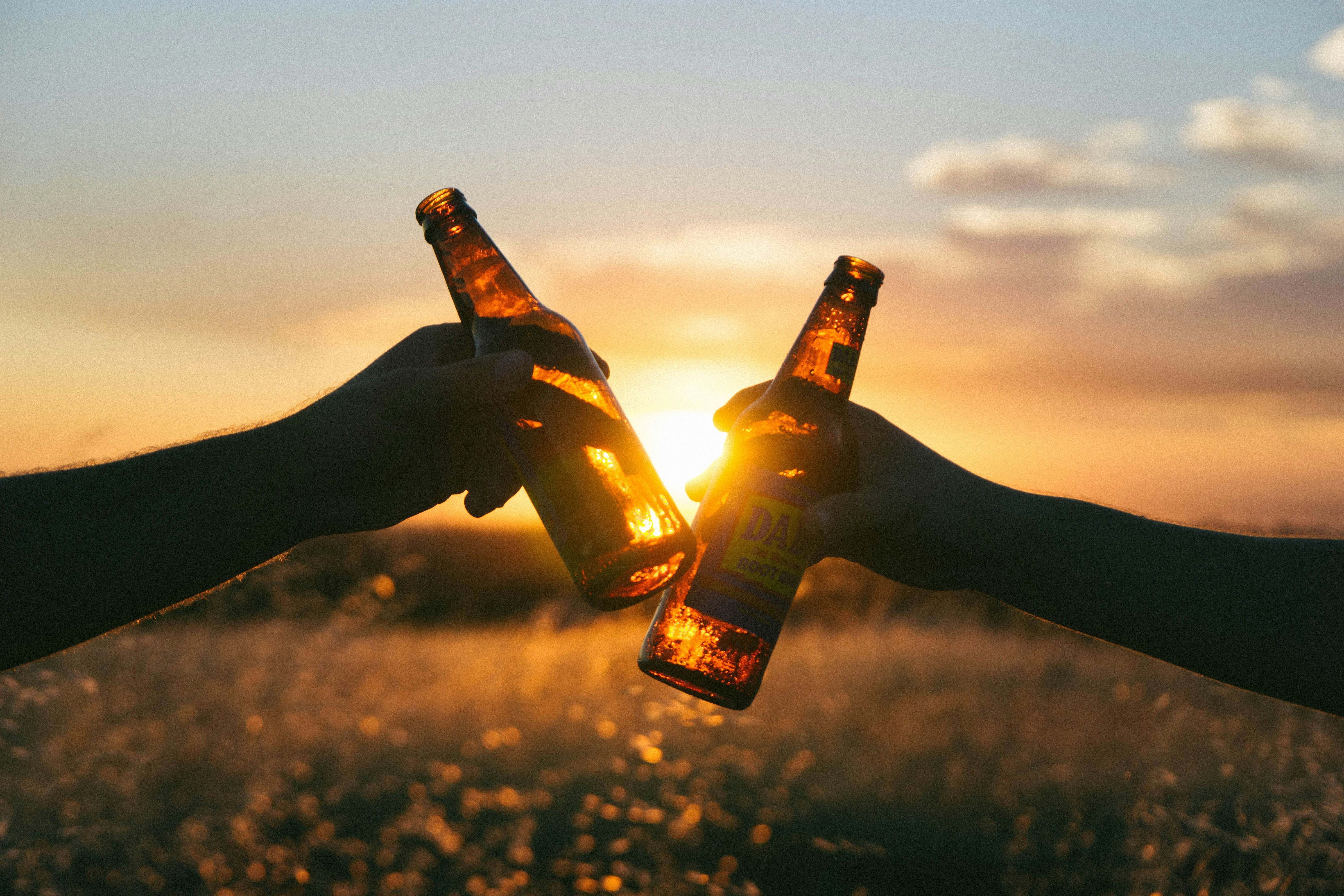 Dos personas chocan su cerveza en medio de una puesta de sol