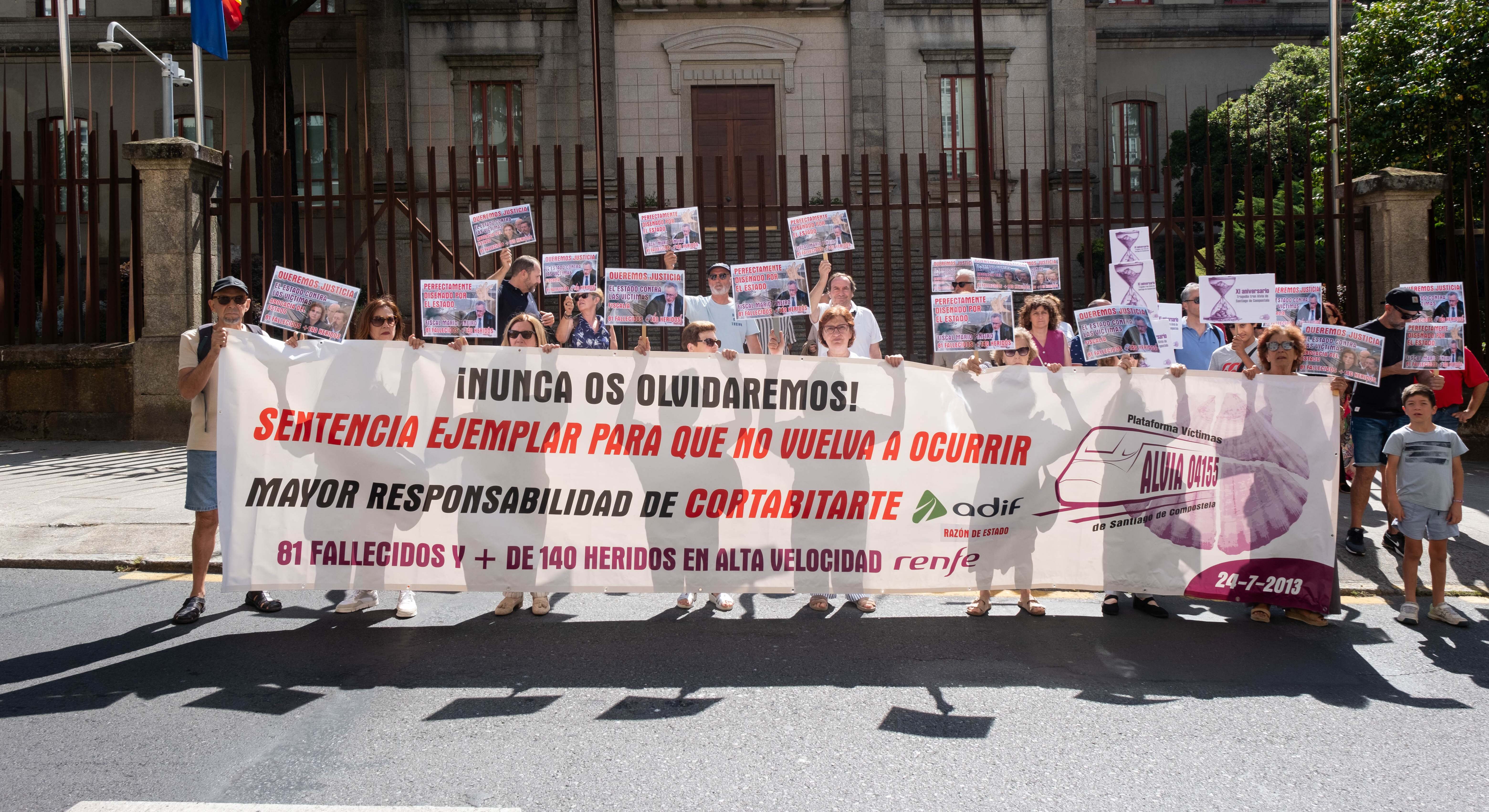 rias personas con una pancarta y carteles durante una concentración de las víctimas de Angrois.