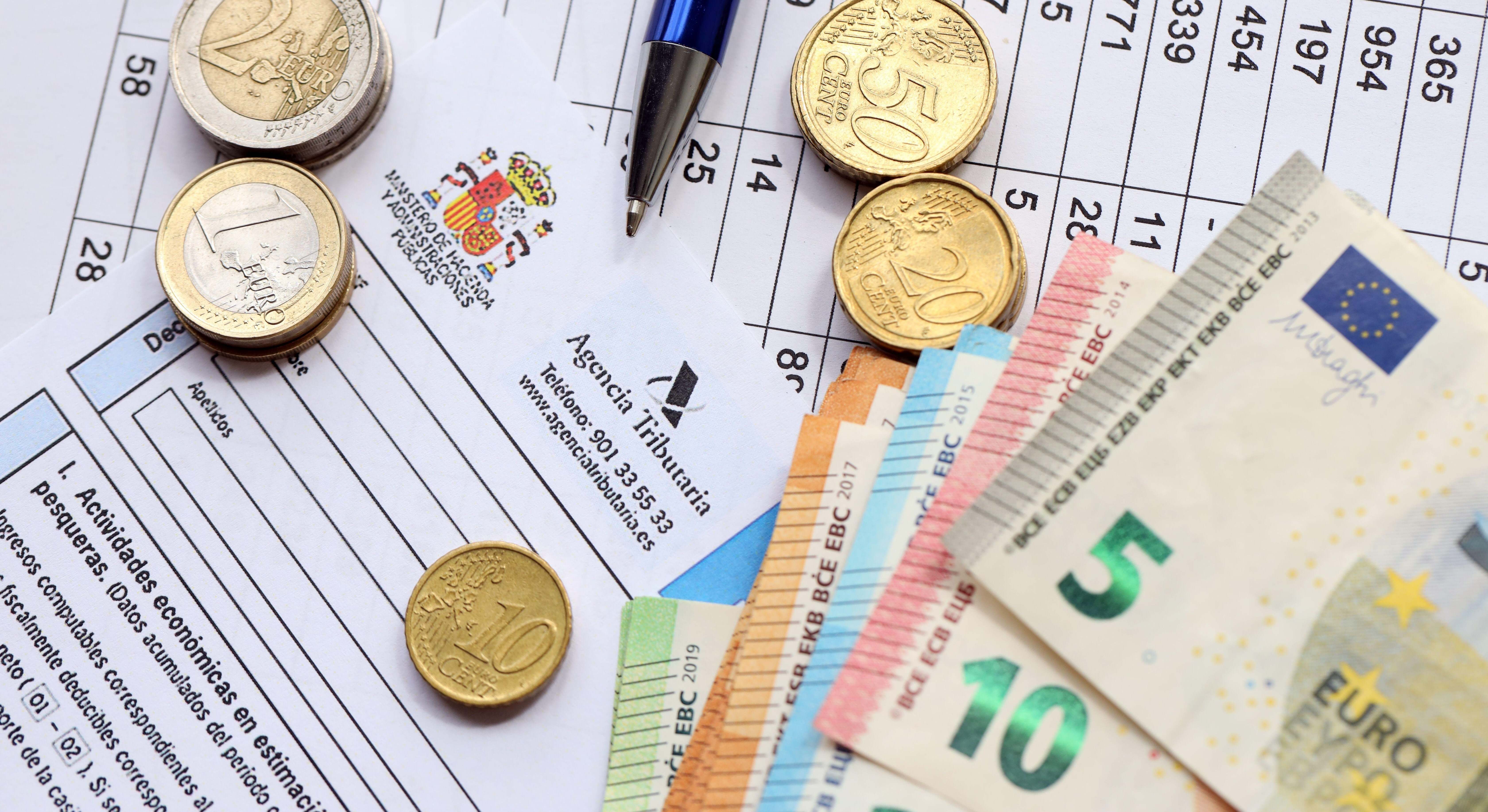 Modelo de declaración de la Agencia Tributaria junto a varias monedas y billetes