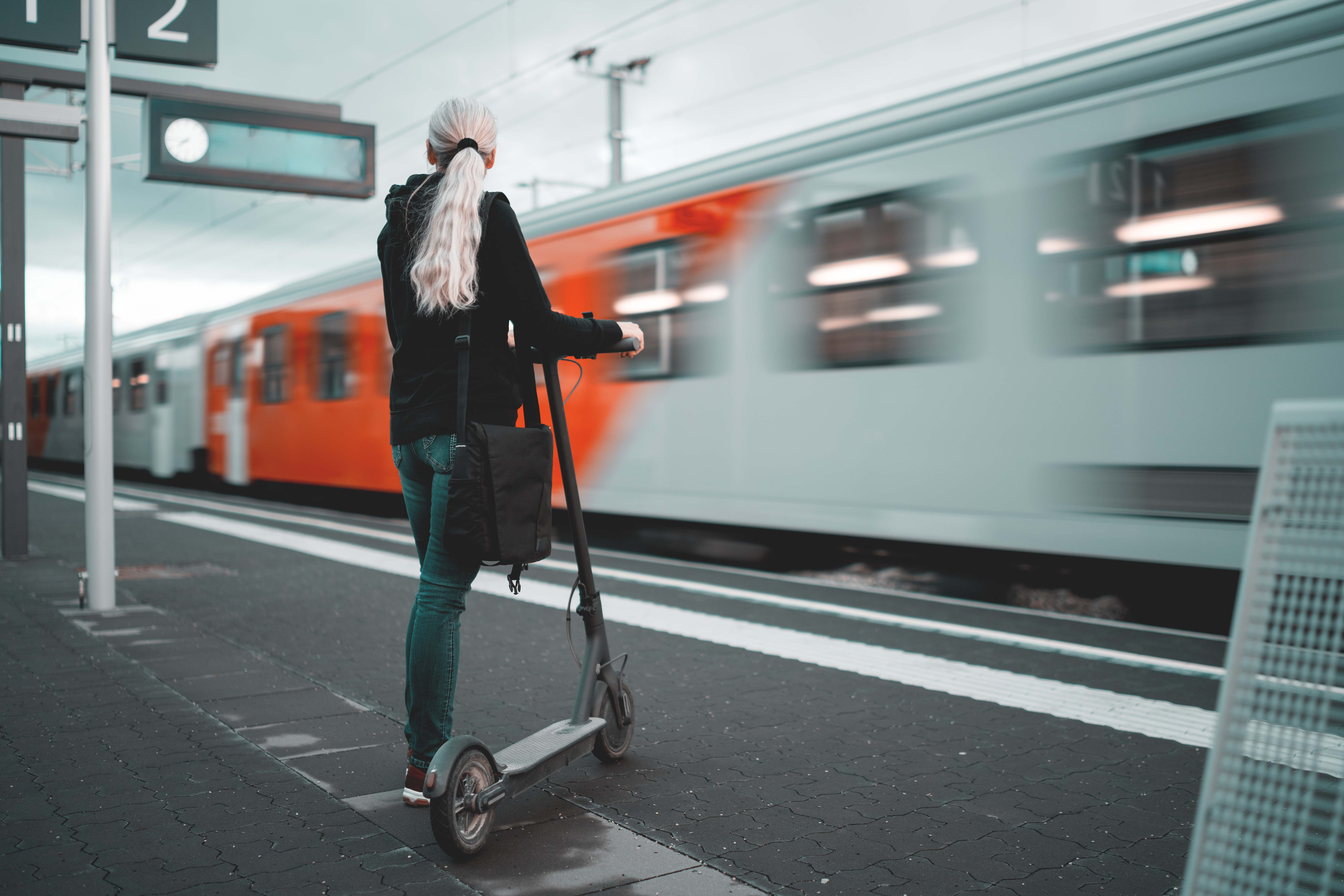 Chica esperando para subir su tren a un patinete.