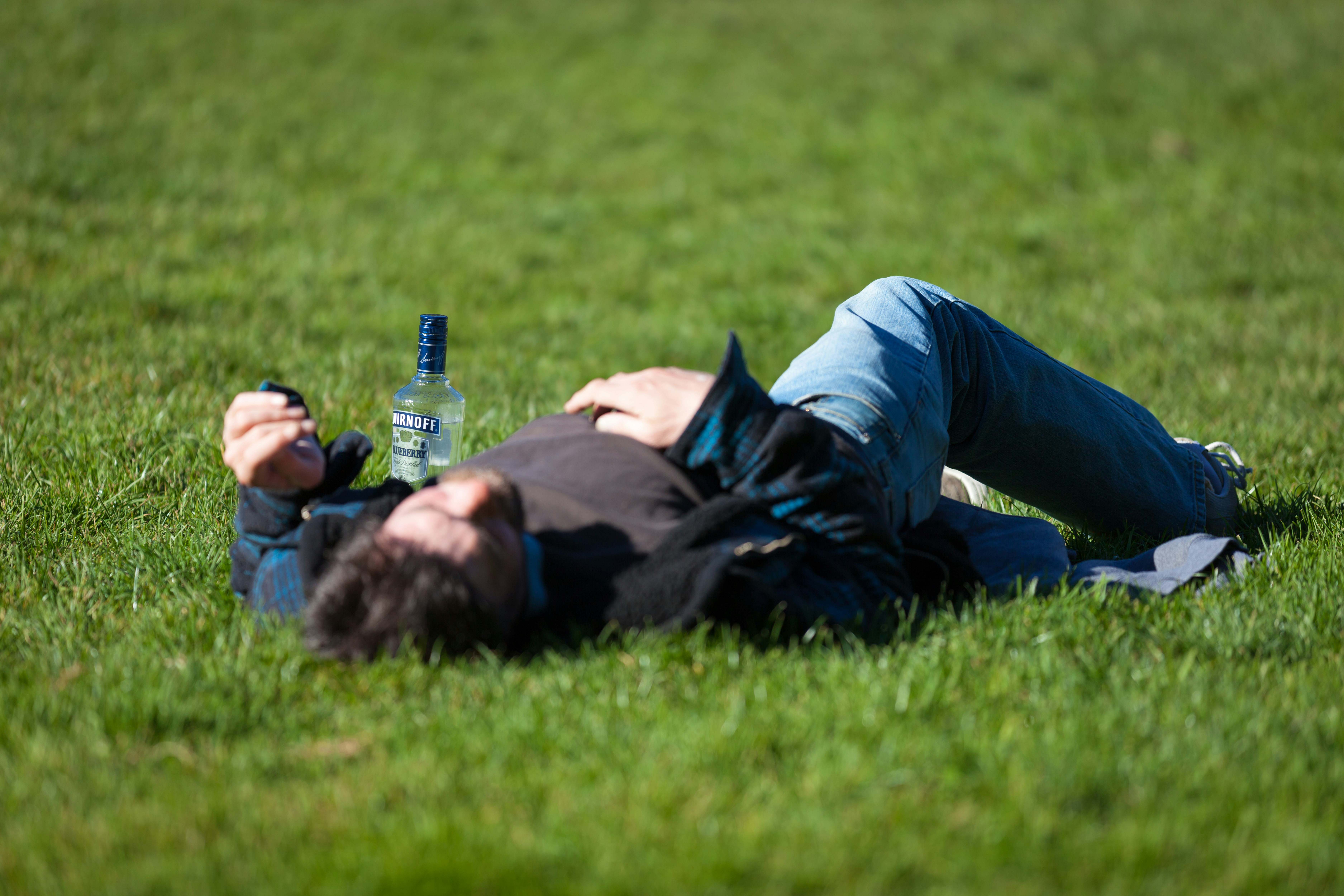 Joven tumbado en el césped con una botella de alcohol