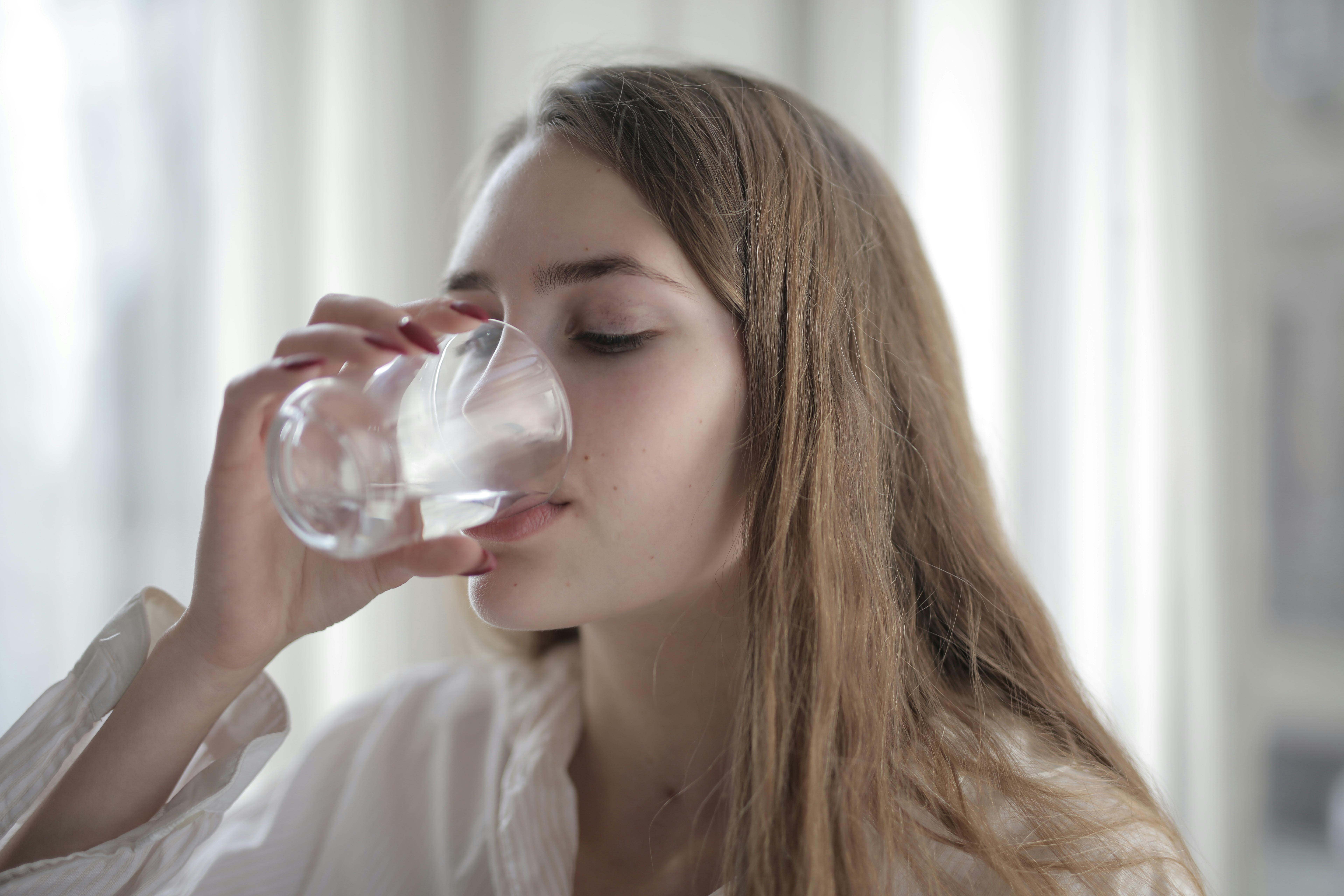 Una persona bebe un vaso de agua en su hogar