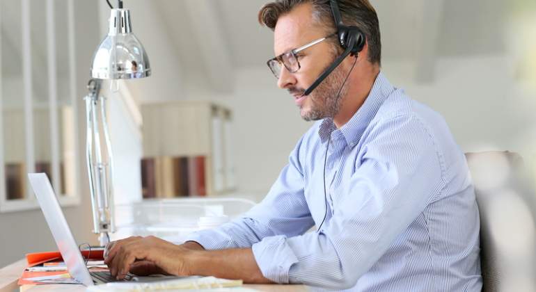 Un hombre teletrabaja con su ordenador y unos auriculares