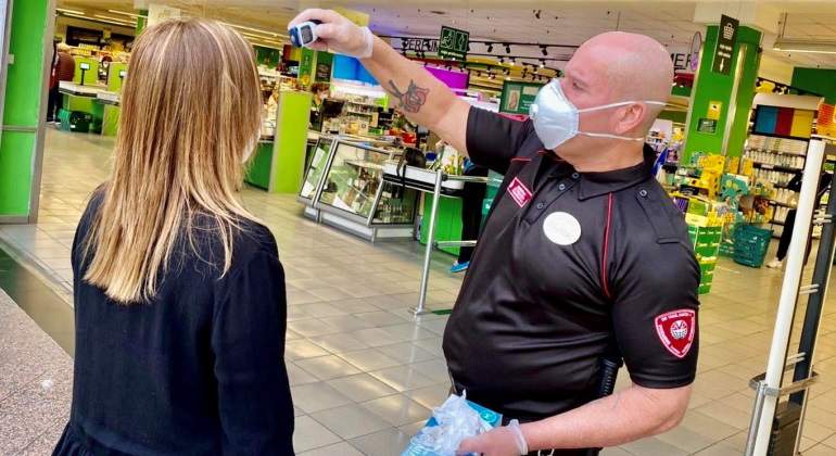 Un empleado de seguridad toma la temperatura a un cliente en el supermercado