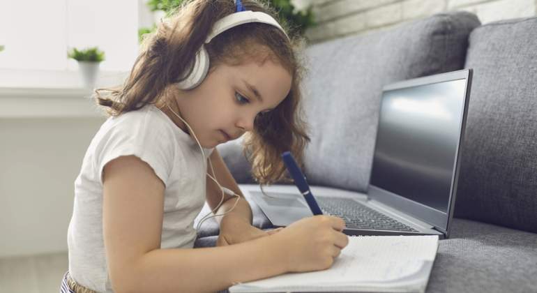 Una nia estudia en casa con auriculares y un porttil