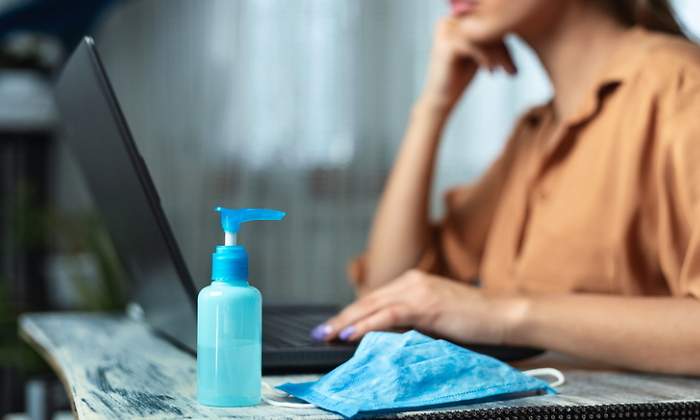Una mujer trabaja con su ordenador con una mascarilla y gel hidroalcohlico en primer plano