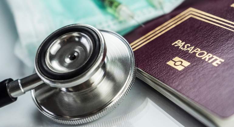 Un fonendoscopio y unas jeringuillas al lado de un pasaporte dando idea de viajar seguro